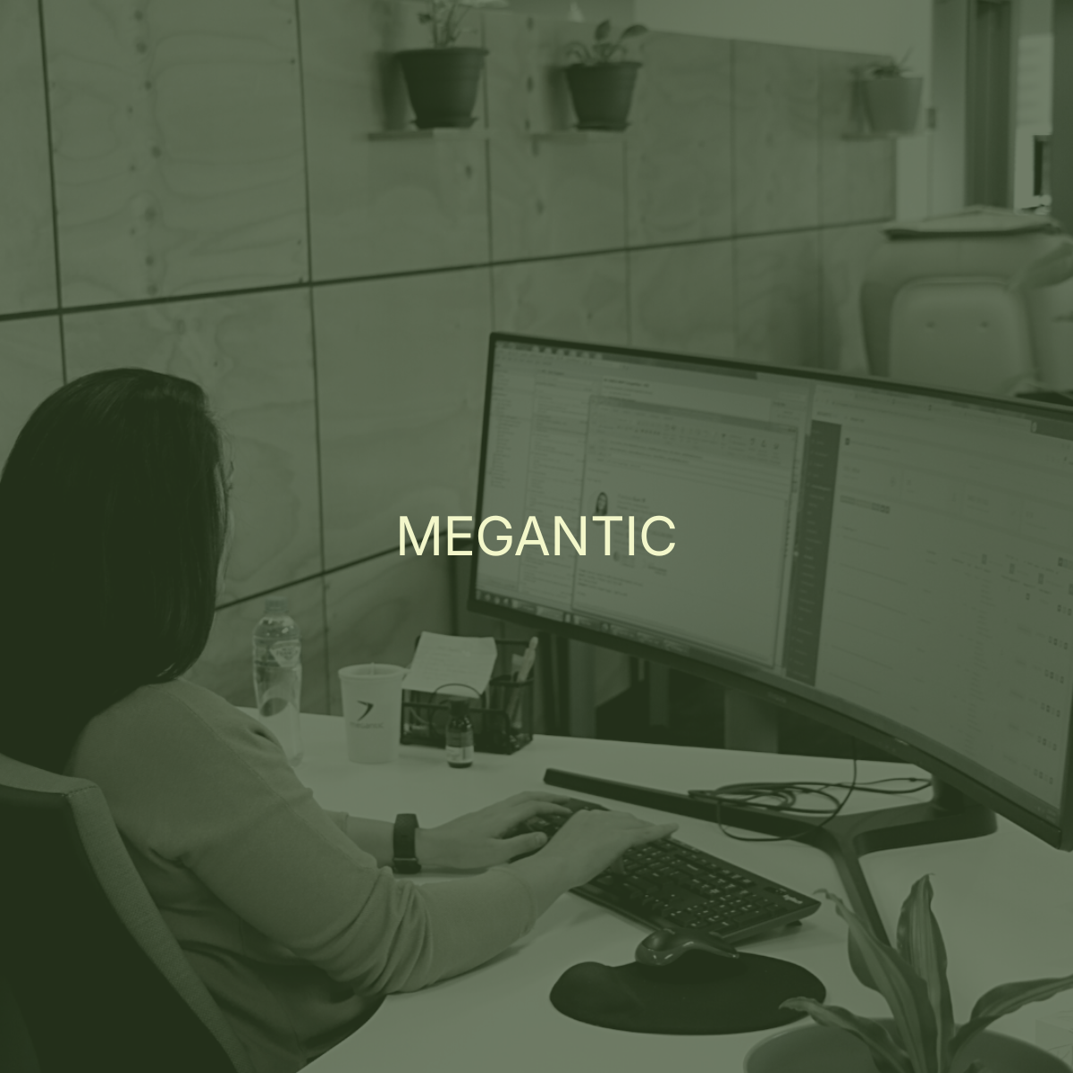 A person working at a desk with a large curved monitor, a keyboard, and a mouse. The desk has a water bottle, a cup, and some papers. Behind the person, there is a wall with wood paneling and a shelf with potted plants. The workspace appears modern and organized.