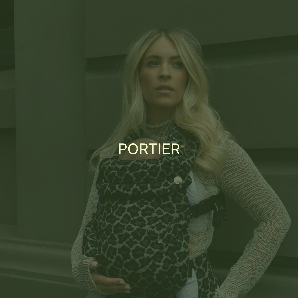 A woman with long blonde hair wearing a beige sweater and a leopard print baby carrier, looking off to the side, standing against a green and brown background.