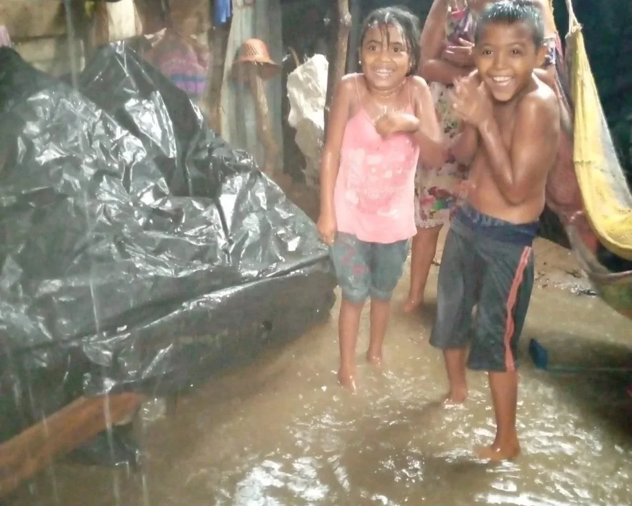 Children playing in a flooded area with muddy water, smiling and wet.