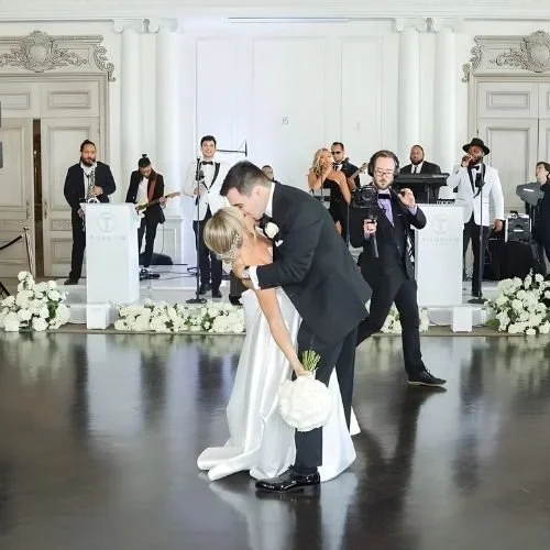 Guests dancing during a wedding reception with live music in New York. A newlywed couple sharing a kiss and the groom holding the bride's bouquet on a dance floor, with a live band playing in the background at a wedding reception in an elegant hall.