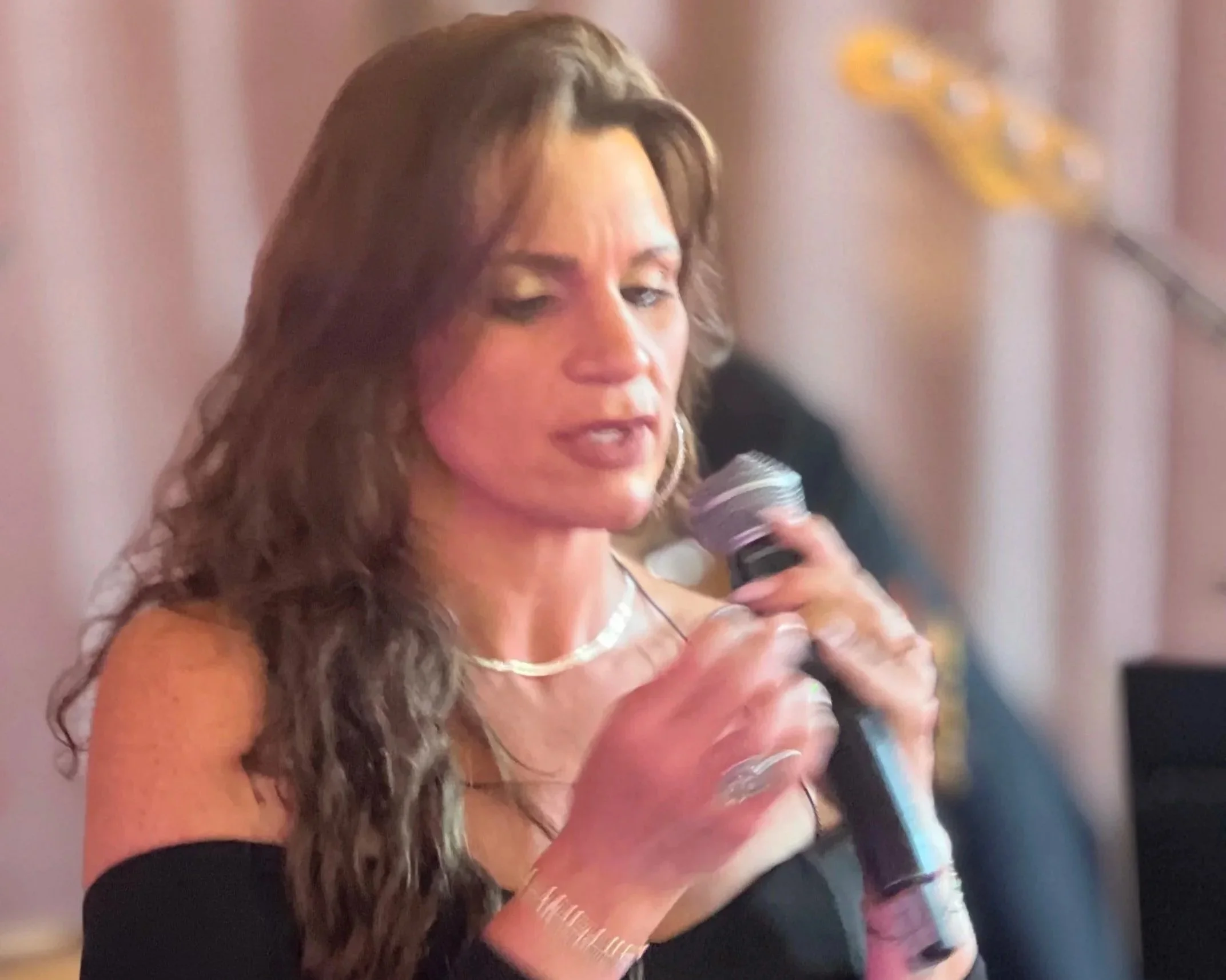 Close-up of a female vocalist with long brown hair, wearing a formal dress at a Wedding in New York holding a microphone, singing at an Wedding.