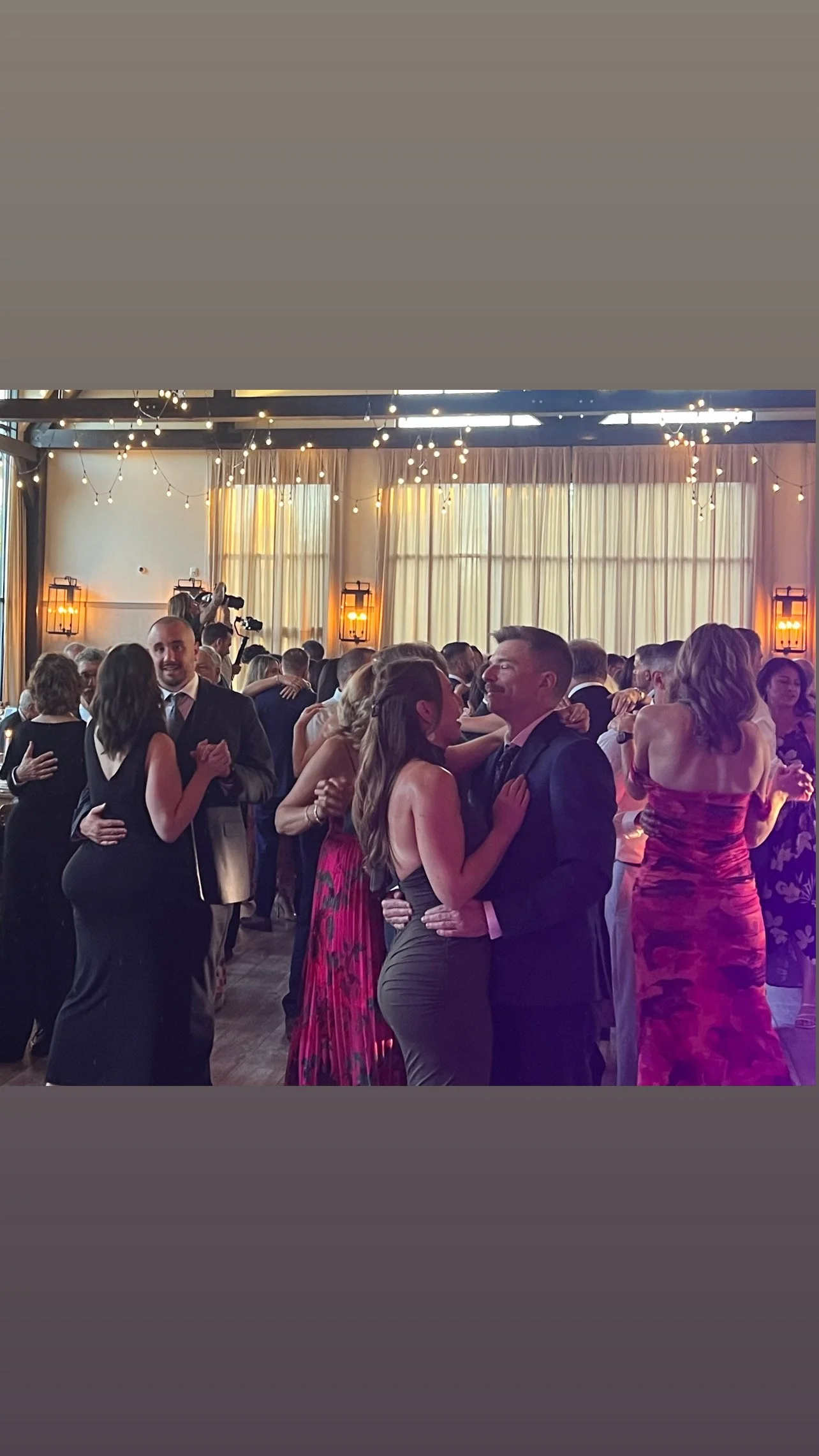 People dancing at a wedding event in a decorated ballroom with string lights and warm lighting.