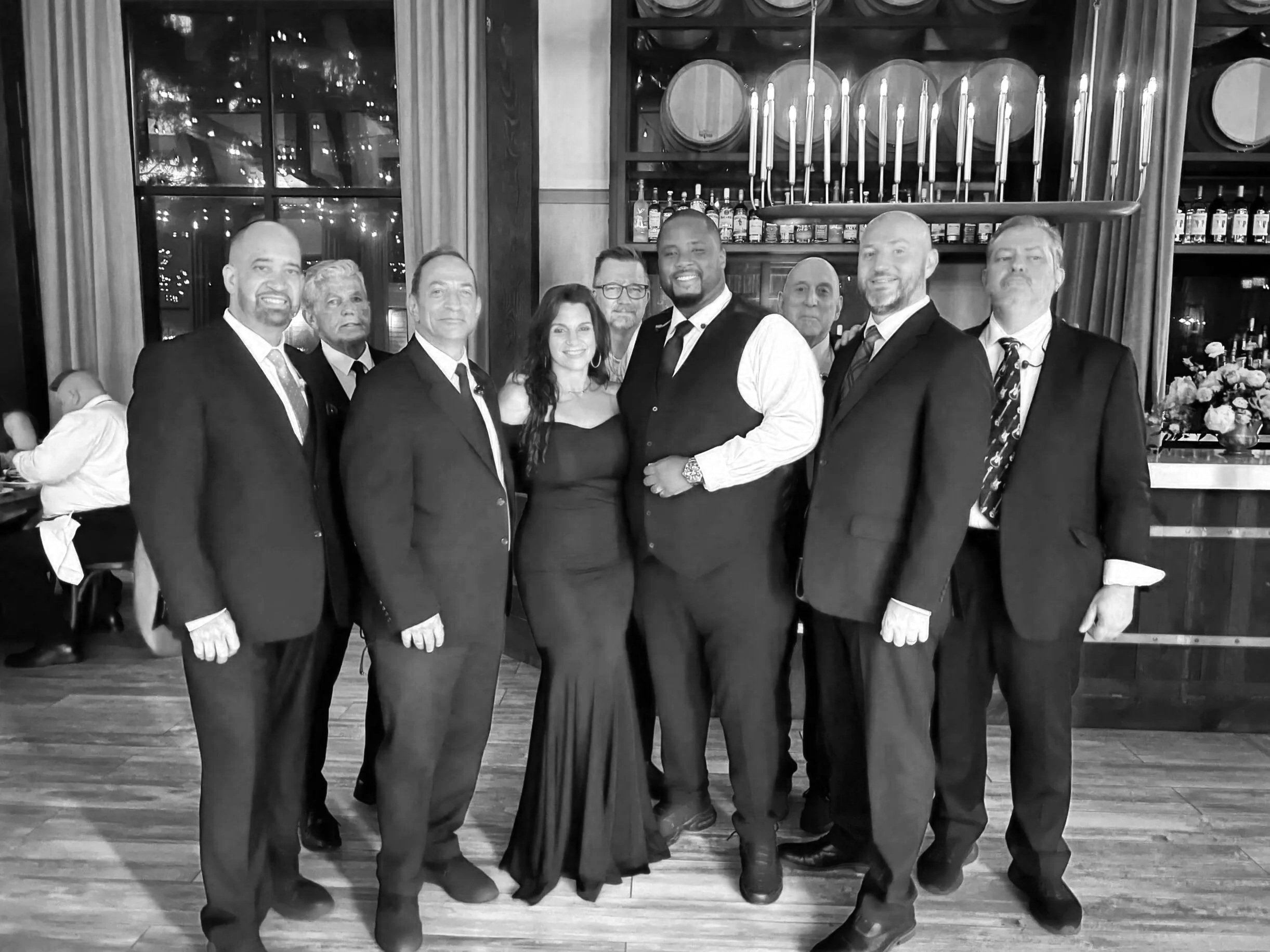 RockSteady Wedding Band dressed in formal attire, posing together indoors in front of a window and shelves with bottles and barrels at a Wedding in a Catering Hall in New York.