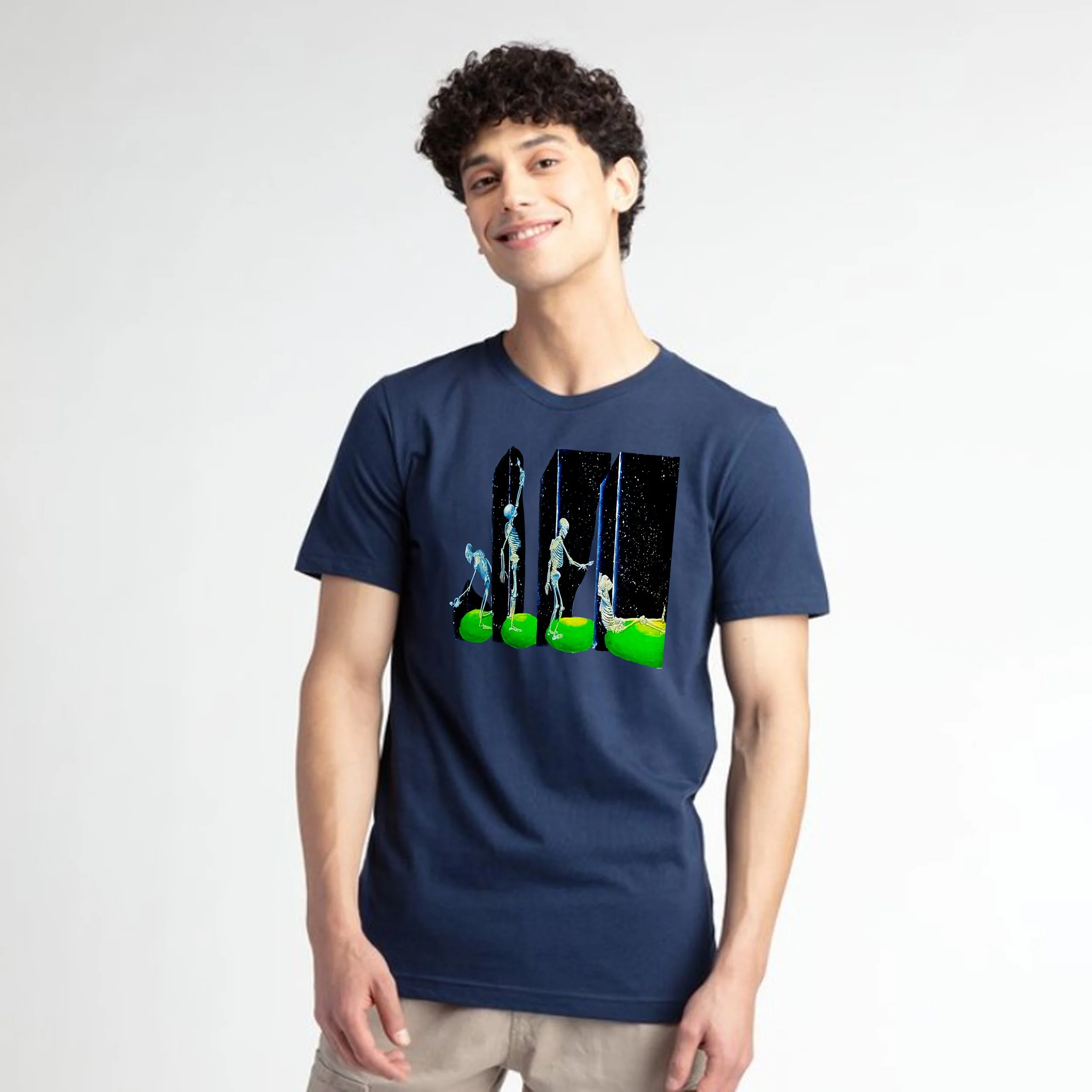 A young man with curly dark hair and a light complexion smiling and wearing a navy blue T-shirt with a graphic design, standing against a plain white background.
