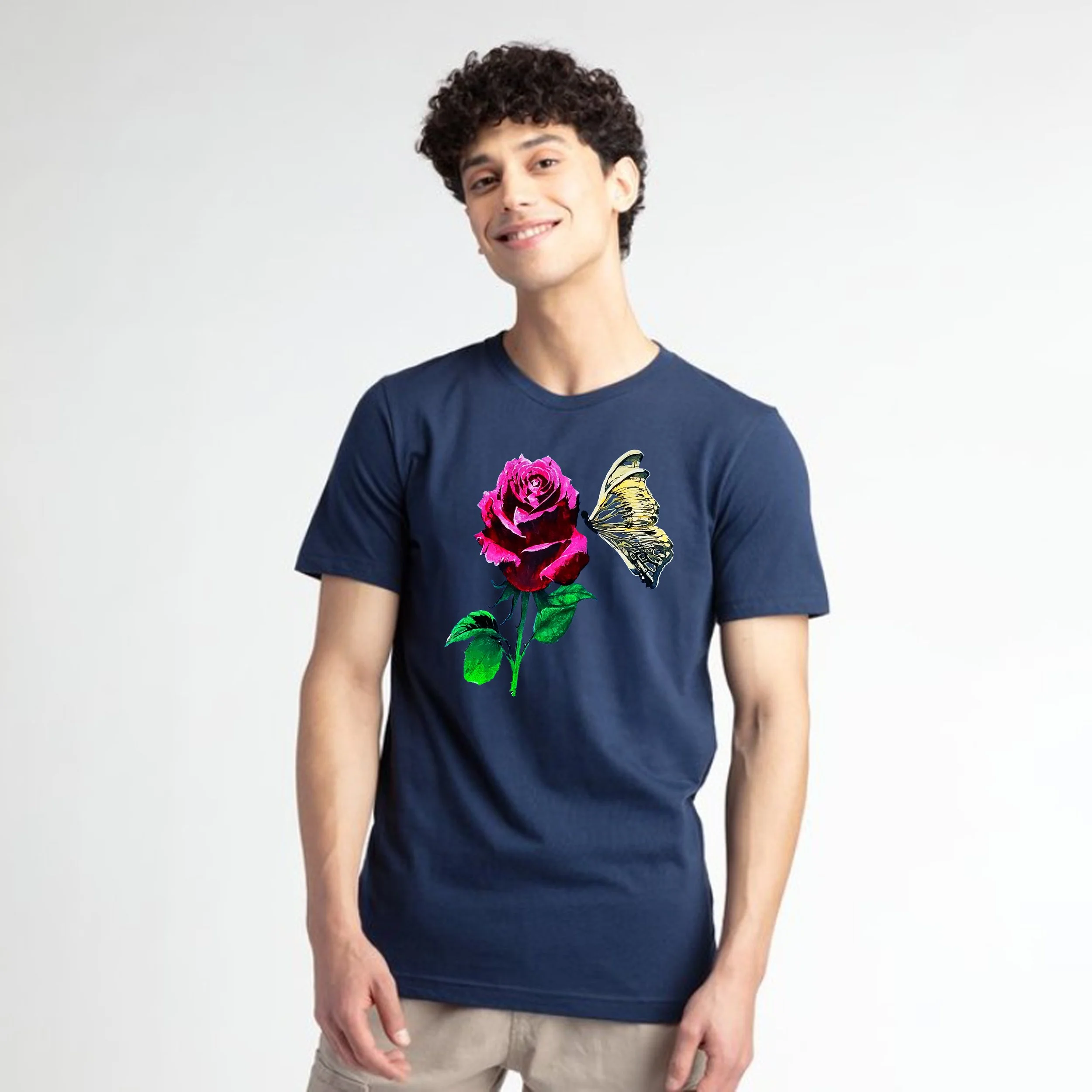 A young man with curly dark hair smiling and wearing a navy blue T-shirt with a colorful floral butterfly graphic, standing against a plain white background.