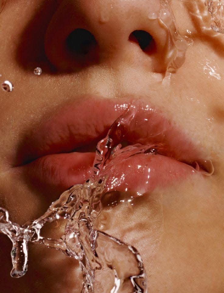 Close-up of a person's lips with water splashing in front of their face, with visible nostrils and skin texture.