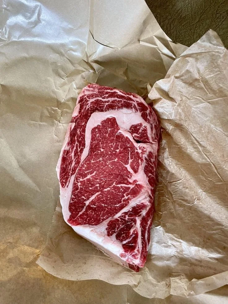 Raw marbled beef steak on parchment paper.