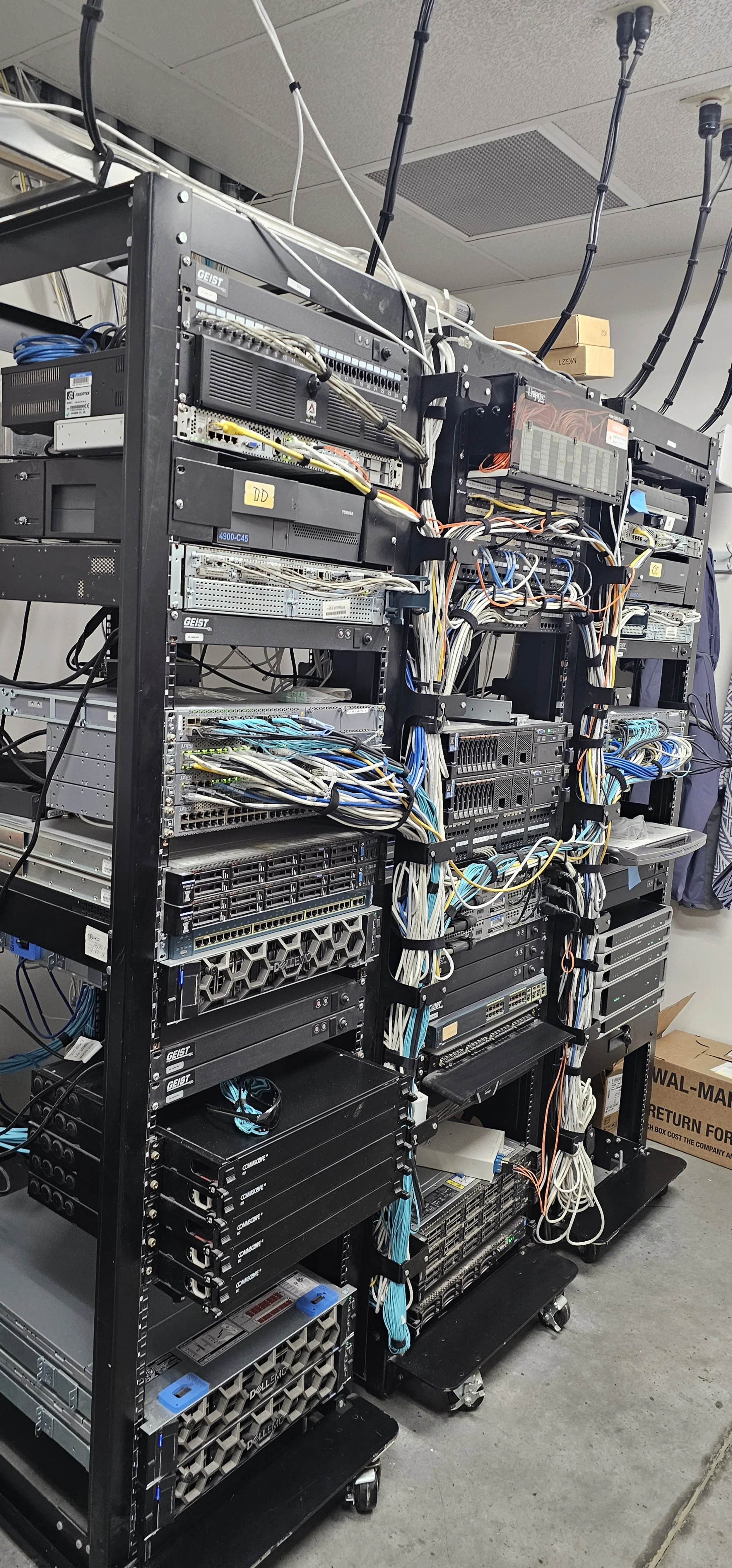 A black server rack filled with networking equipment, cables, and hardware components in a data center room.