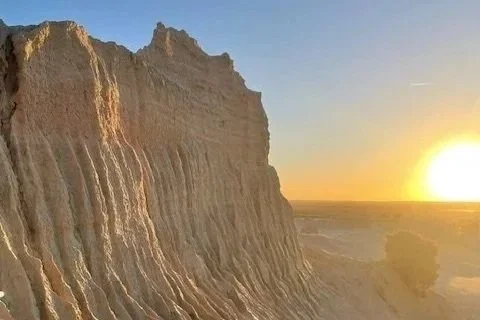 Cliffs at sunset with a view of the horizon and the sun setting over a flat landscape.