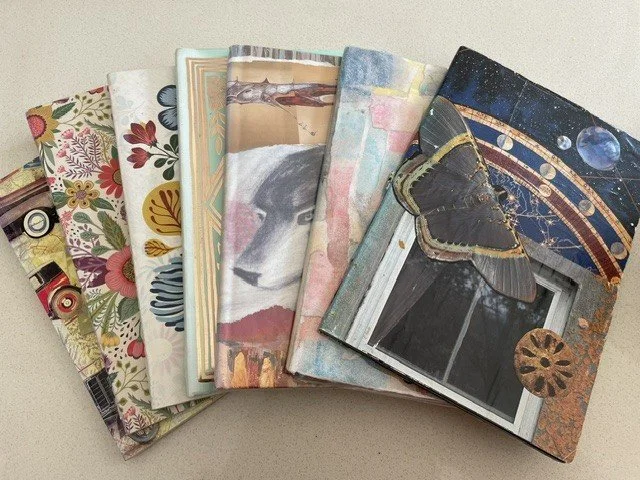 A collection of books with collage covering scattered across a tabletop.