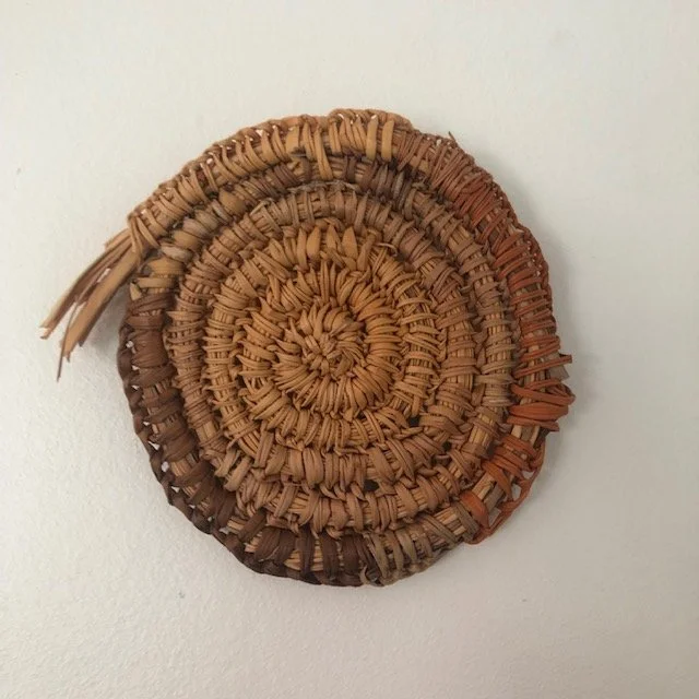 Close-up of a coiled, woven straw or rattan decorative object against a plain white background.