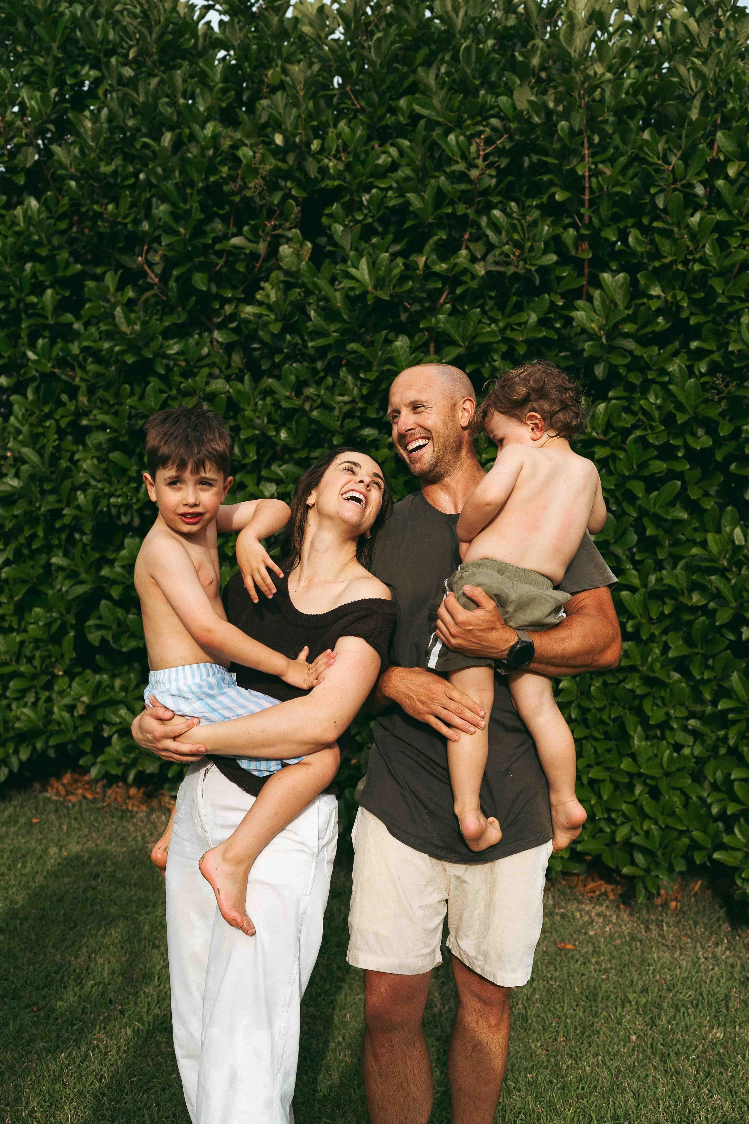 A family playing with their children in a backyard with a hedge and trees.