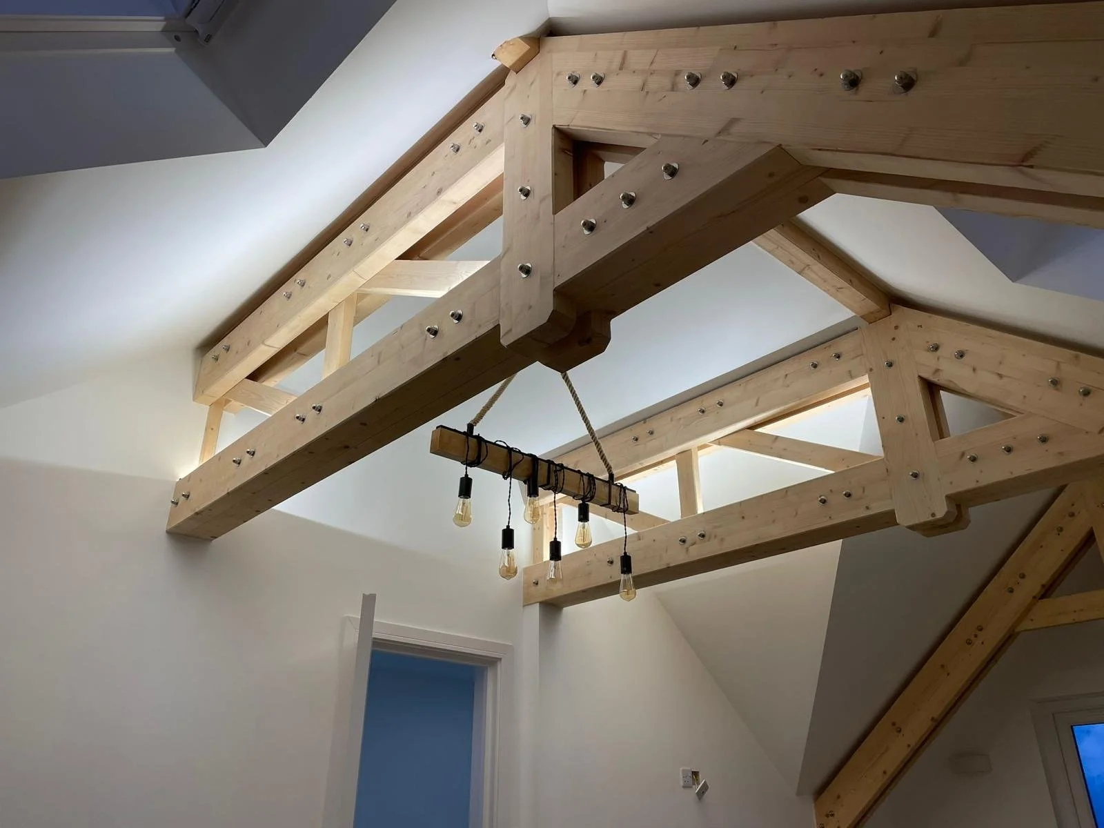 Interior view of exposed wooden beams and a hanging chandelier with light bulbs in a room with sloped ceiling.