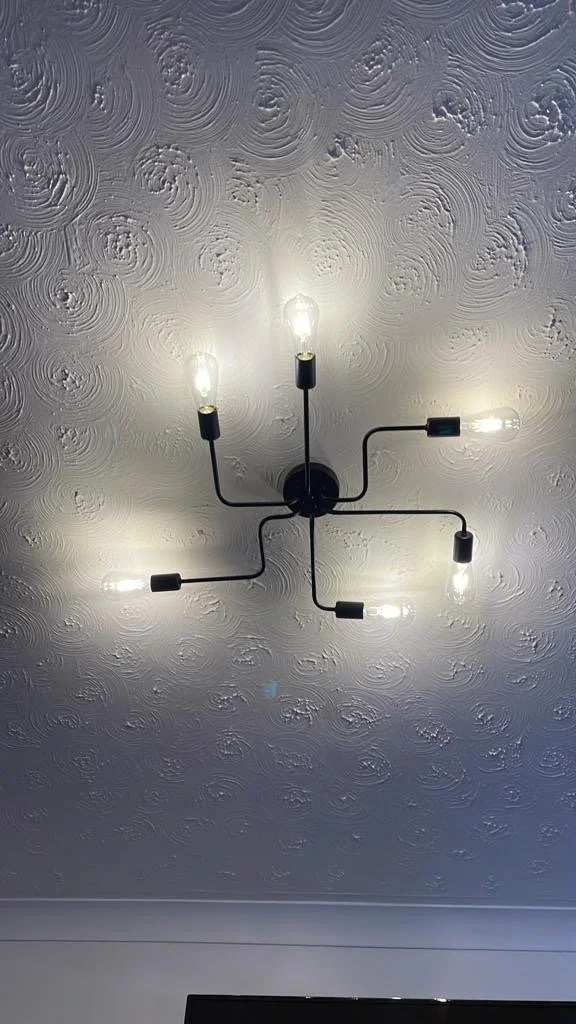 Ceiling light fixture with six exposed bulbs attached to black arms, mounted on a textured ceiling with swirling patterns.