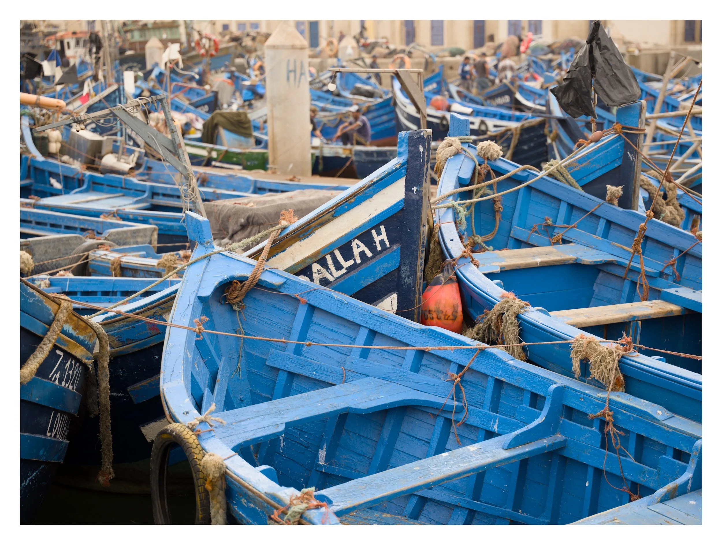 A crowded dock with numerous blue boats tied together, some with ropes, fenders, and fishing gear visible.
