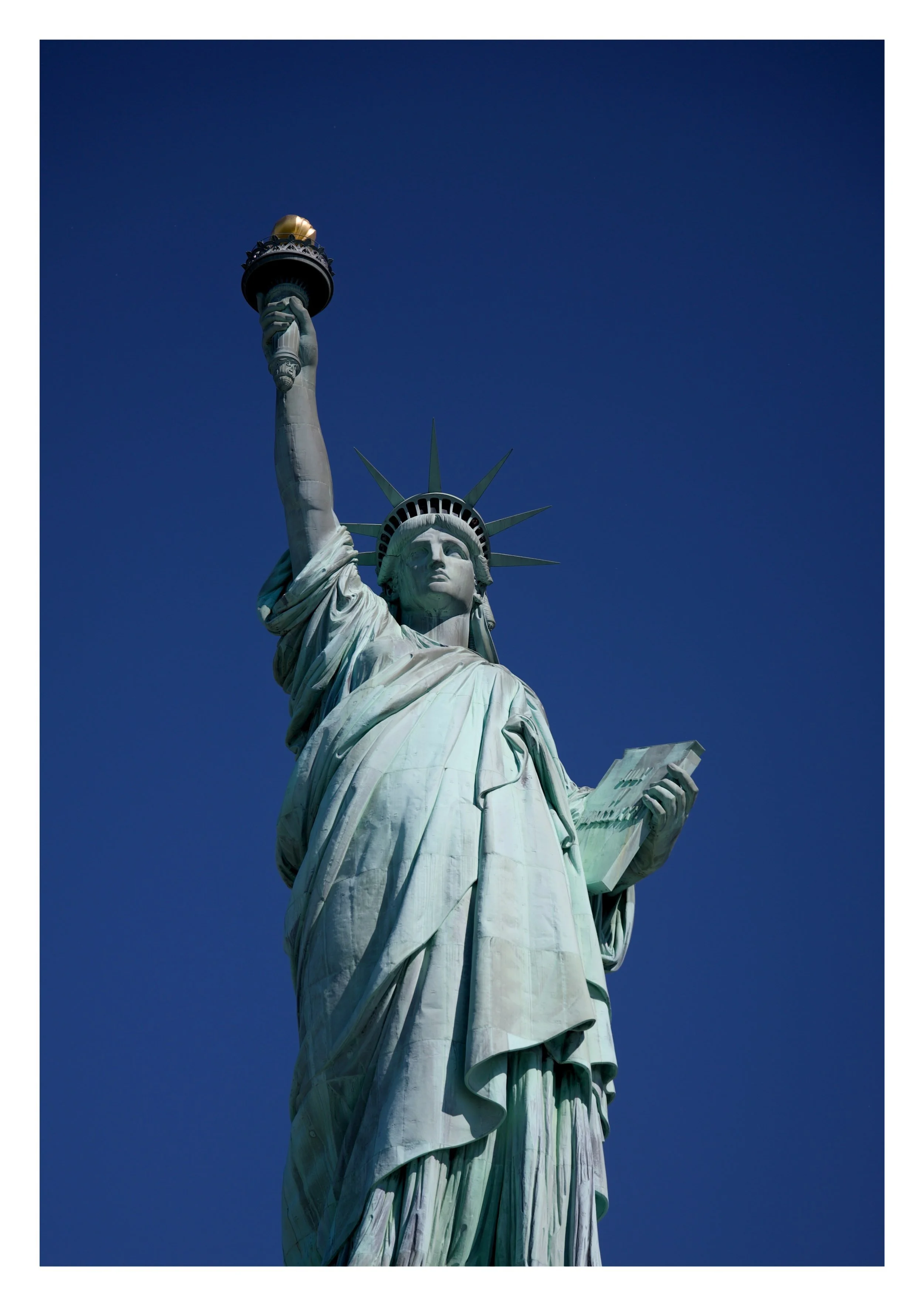 Close-up of the Statue of Liberty's head, torch and upper body against a clear blue sky.