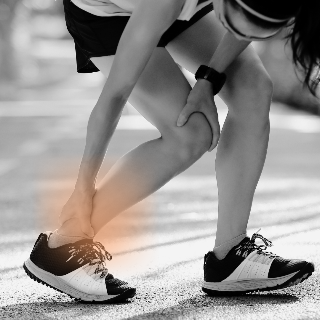 A woman wearing athletic shoes, bent over, holding her knee in pain on an outdoor running track.