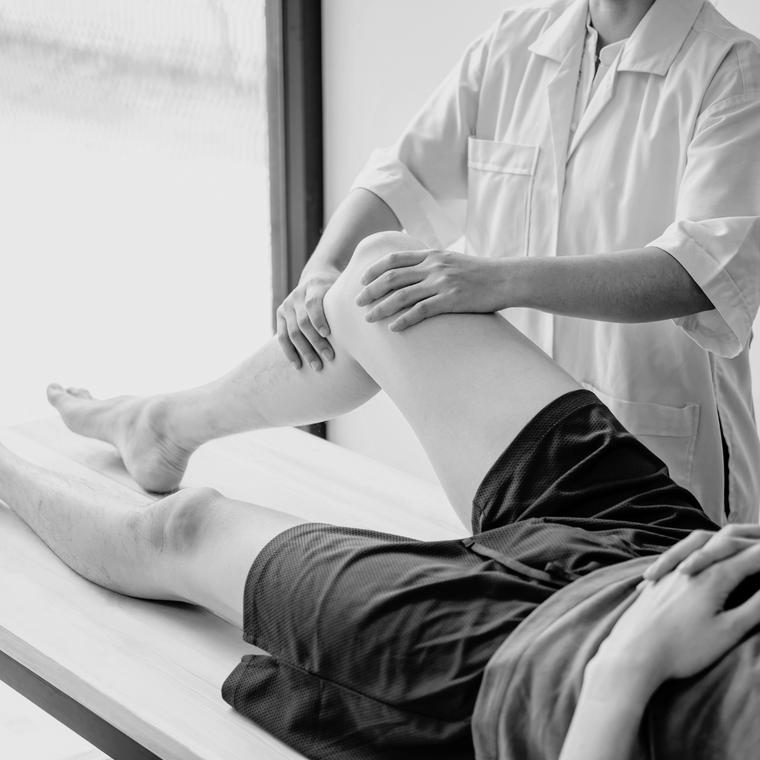 A medical professional is examining a patient's leg in a clinical setting.