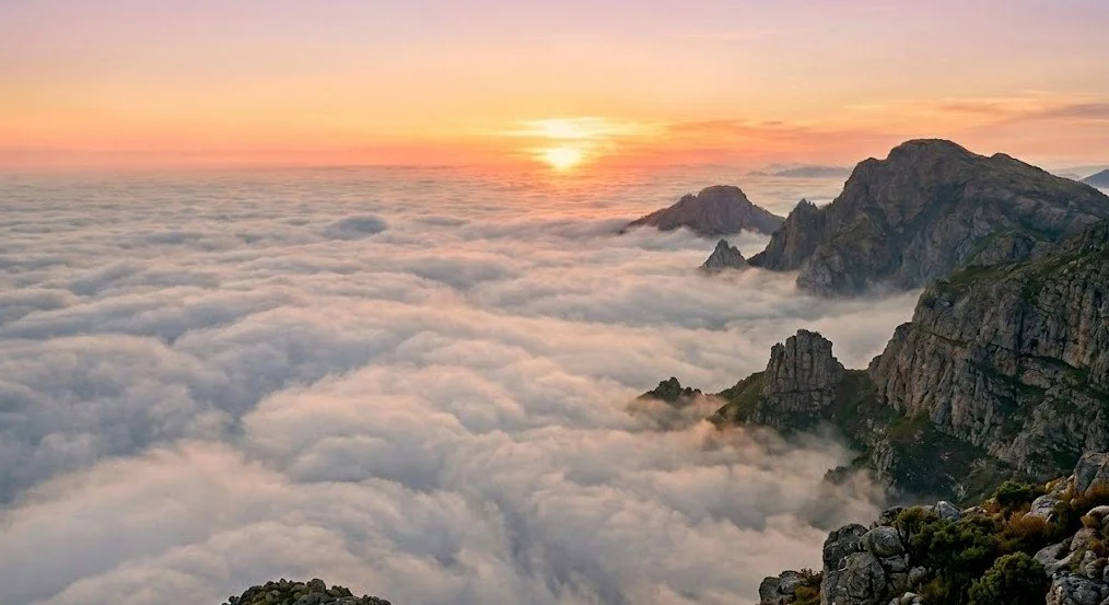 Sunrise over a mountain range with clouds filling the valleys below.