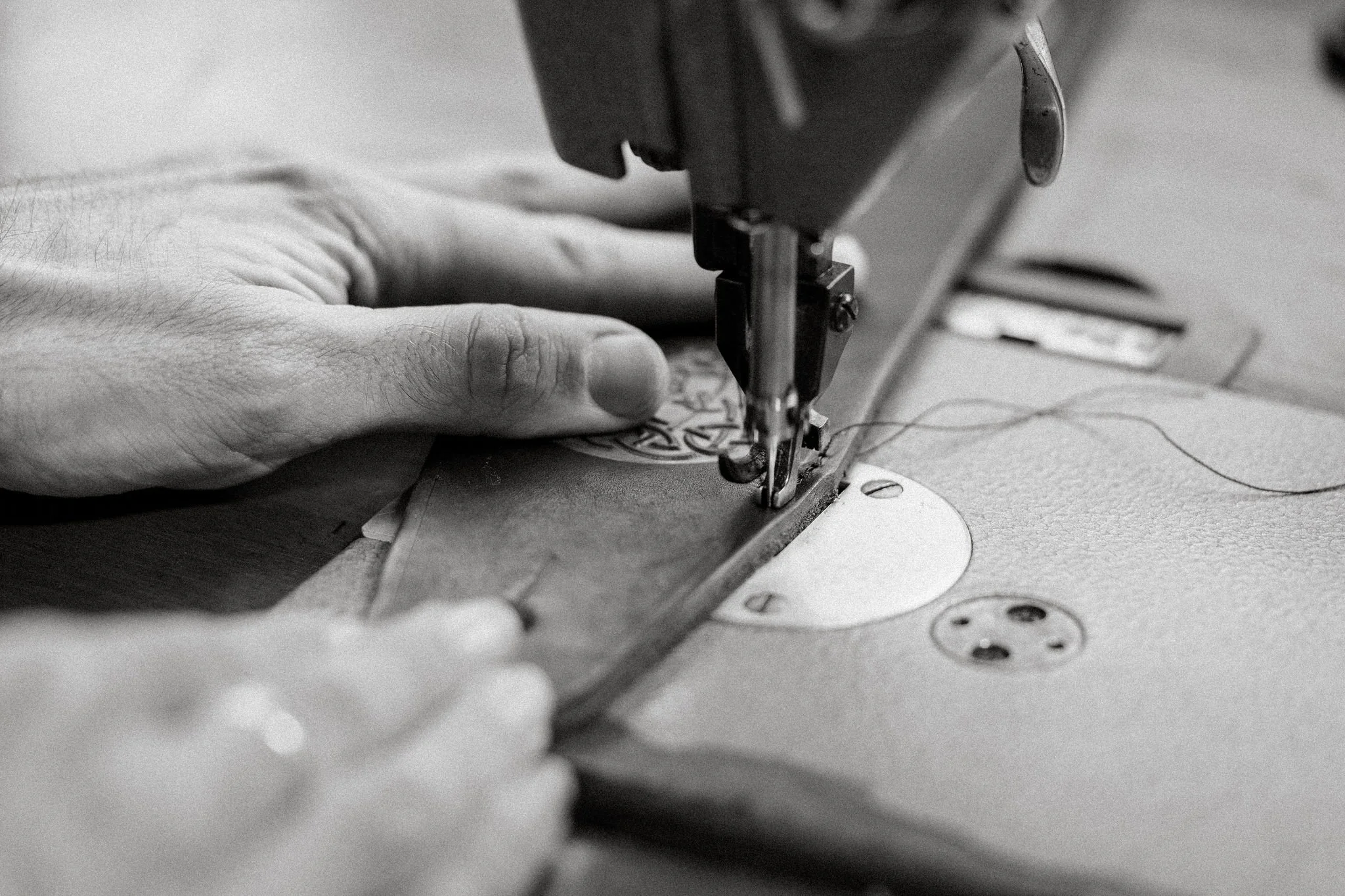 Close-up of a sewing machine with a person's hand guiding leather under the needle.
