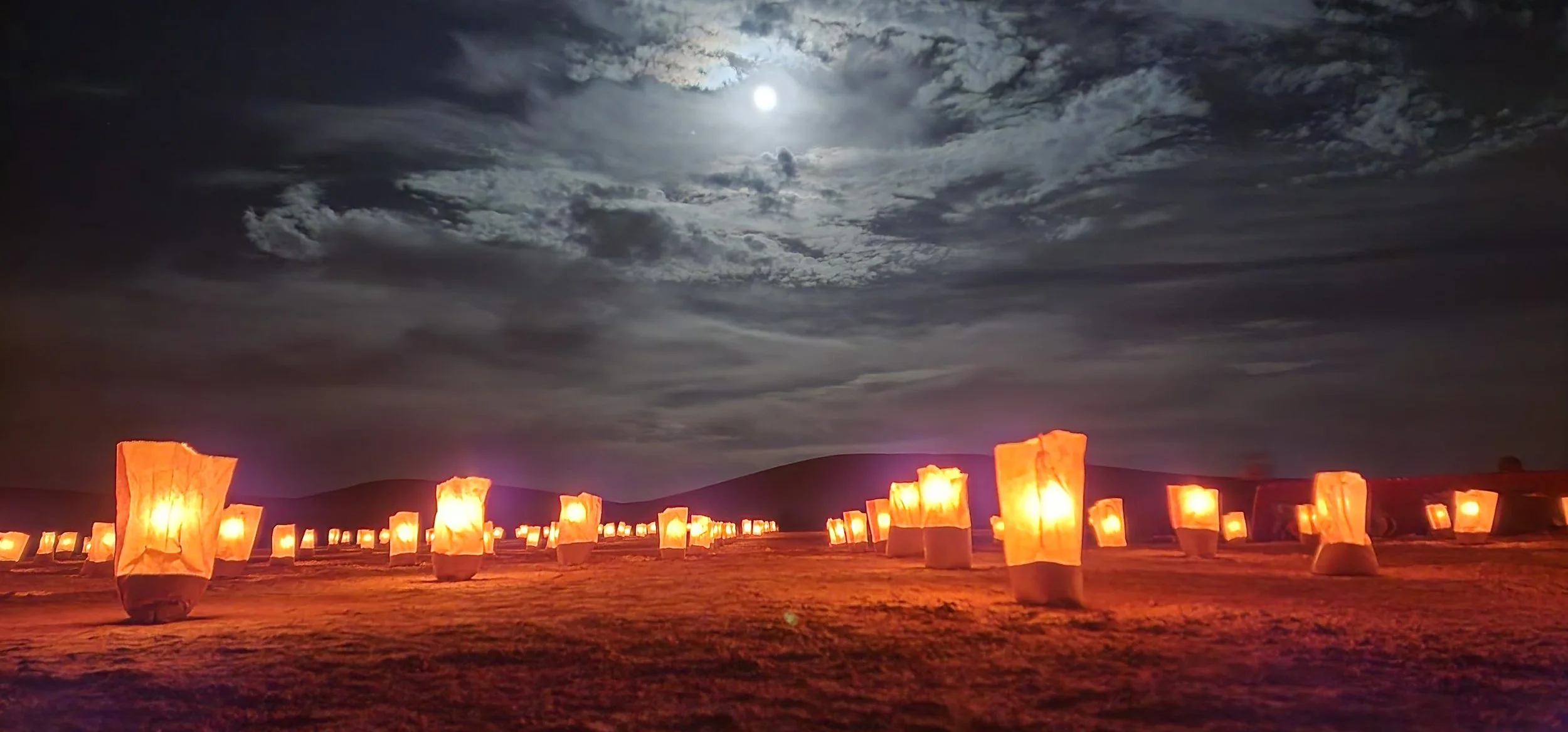 Lune pleine dans un ciel nuageux nocturne dans le désert. Sur le sol, il y a des lampions en papier orange allumés.