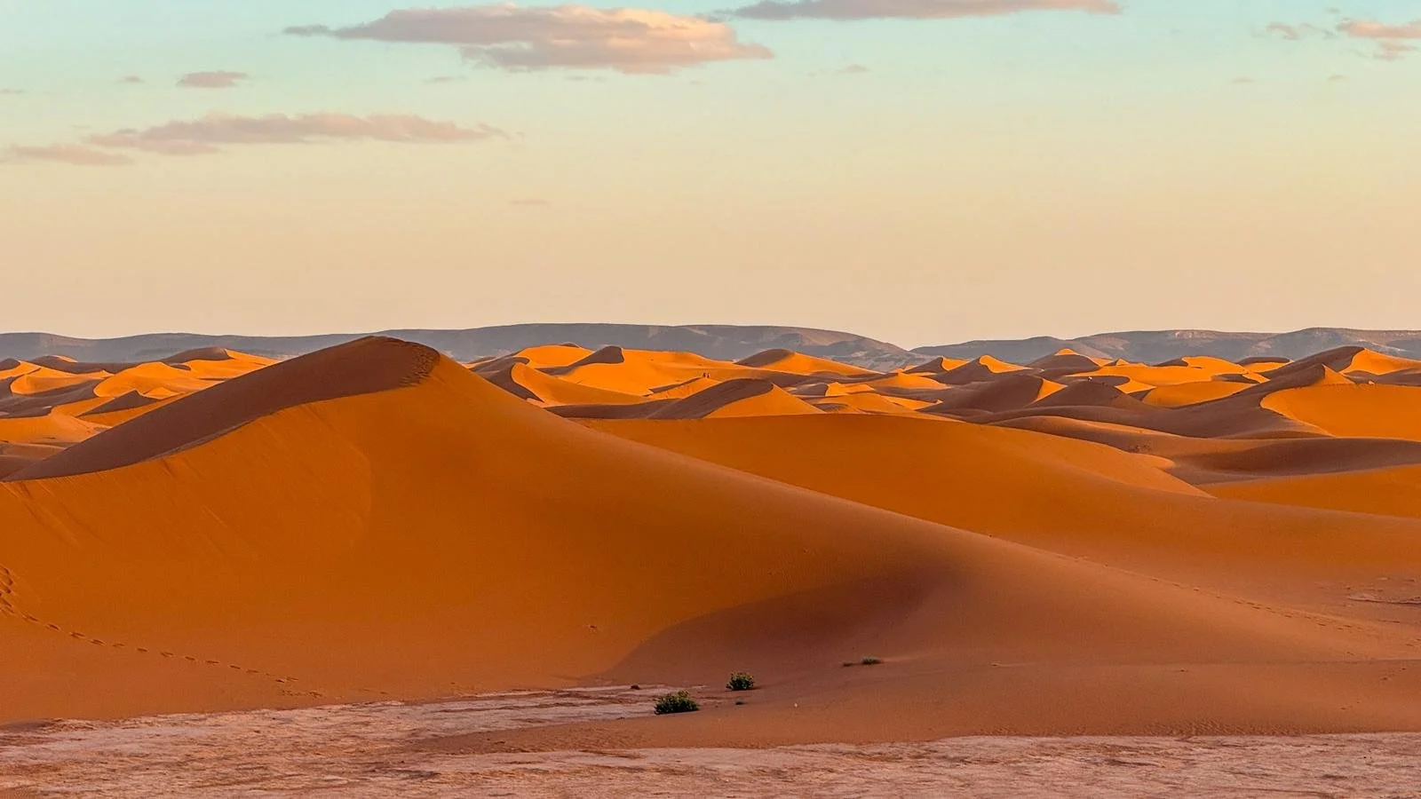 Dunes de sable dans un désert avec un ciel légèrement nuageux, couleur chaude et ambiance paisible.