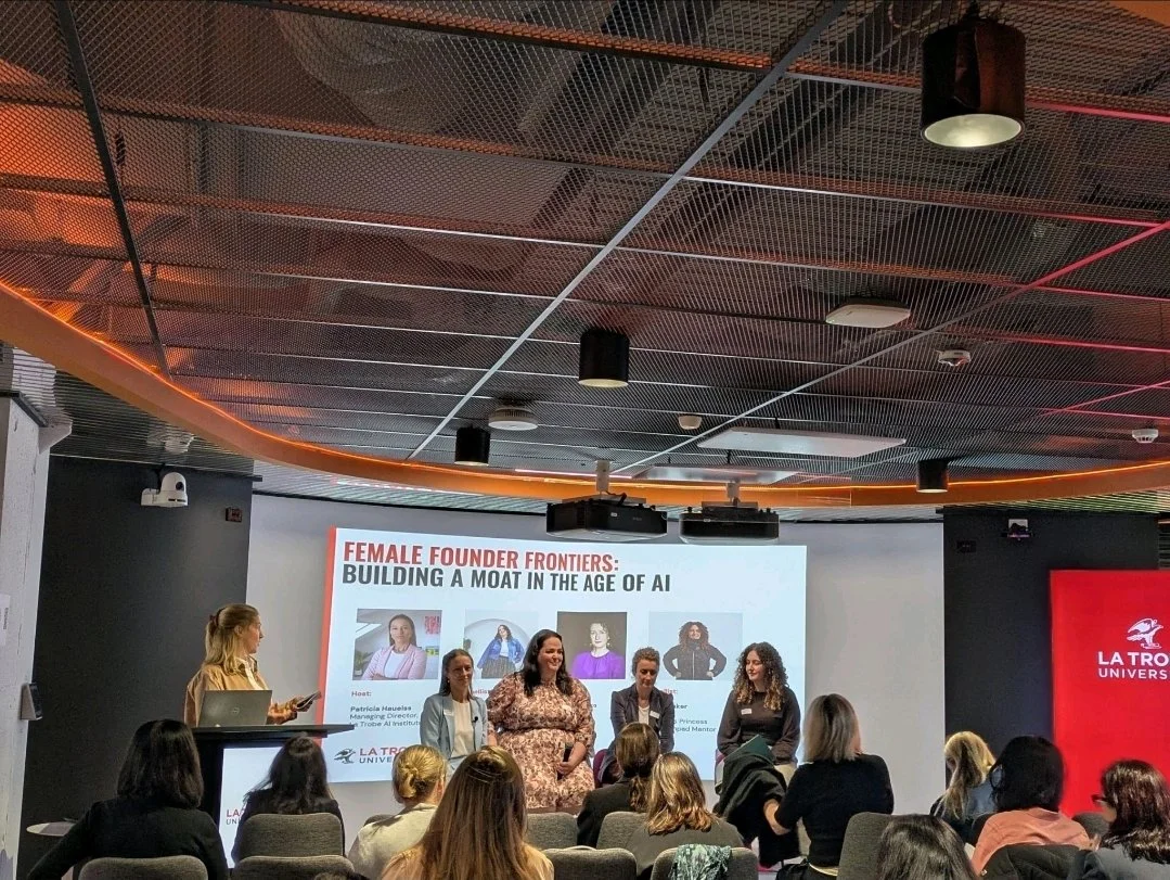 Panel discussion at La Trobe University featuring four women on stage, with a presentation slide behind them titled 'Female Founder Frontiers: Building a Moat in the Age of AI.' Audience seated facing the panel.
