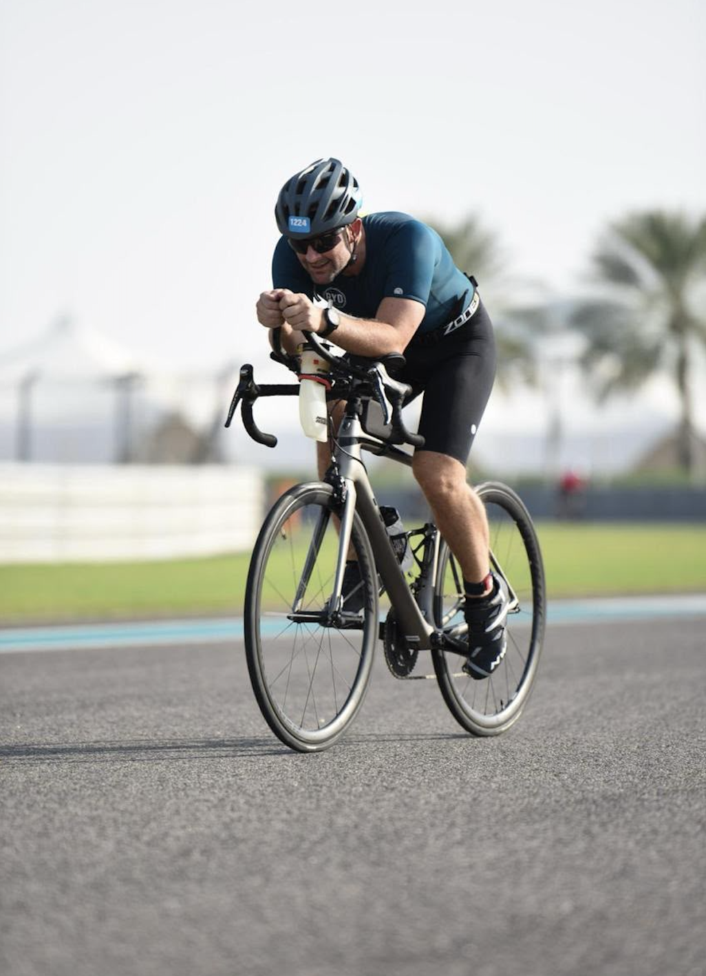 Male cyclist in a blue shirt, black shorts, and a helmet riding on a race track.