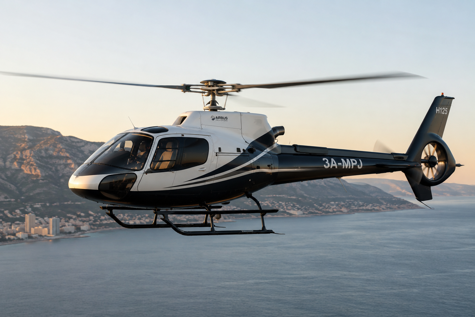 A helicopter flying over water with mountains and a city in the background during sunset.