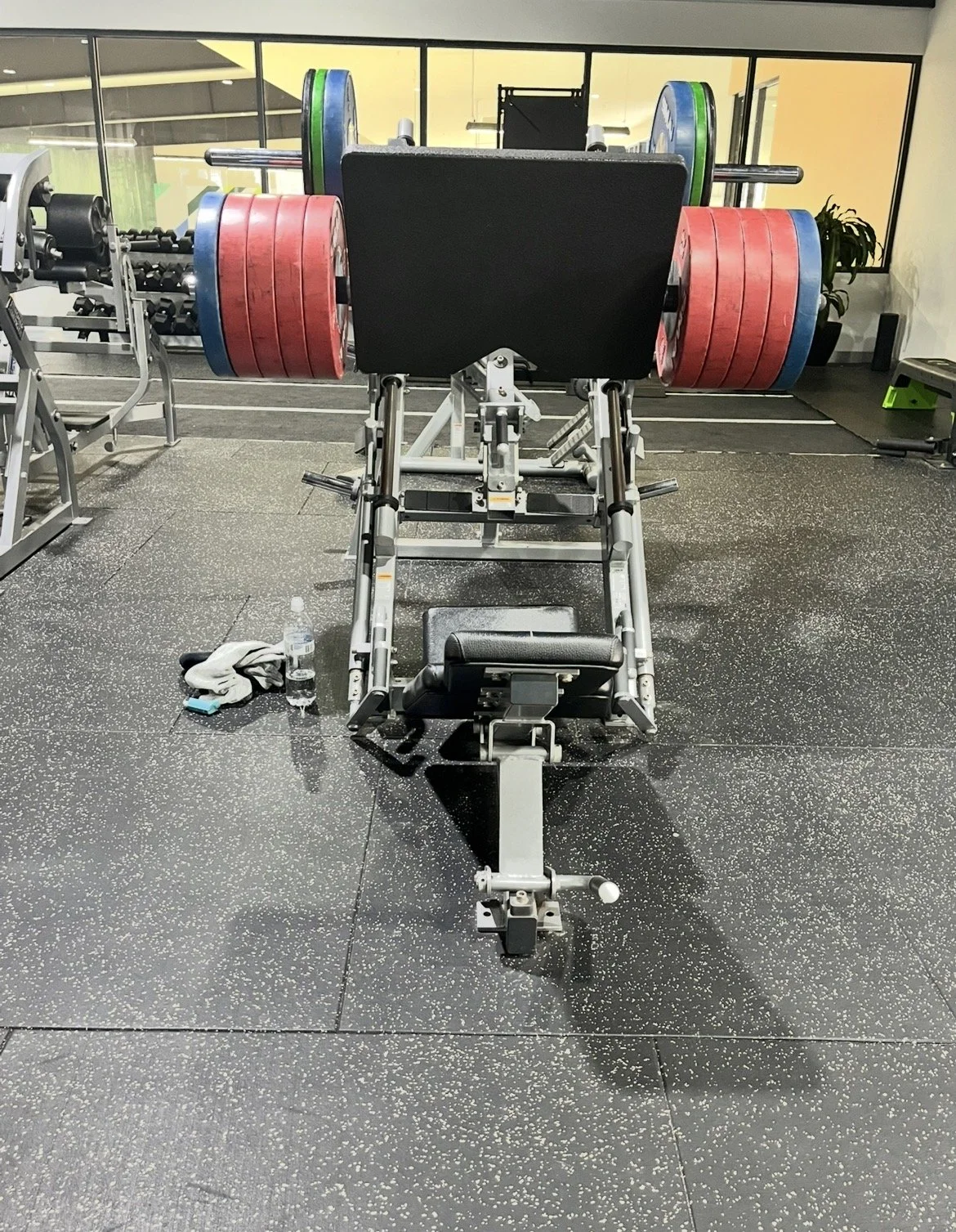 An angled leg press with a loaded with weight plates in red, green, and blue, in a gym with black flooring and large windows, demonstrating our ability to push through resistance.