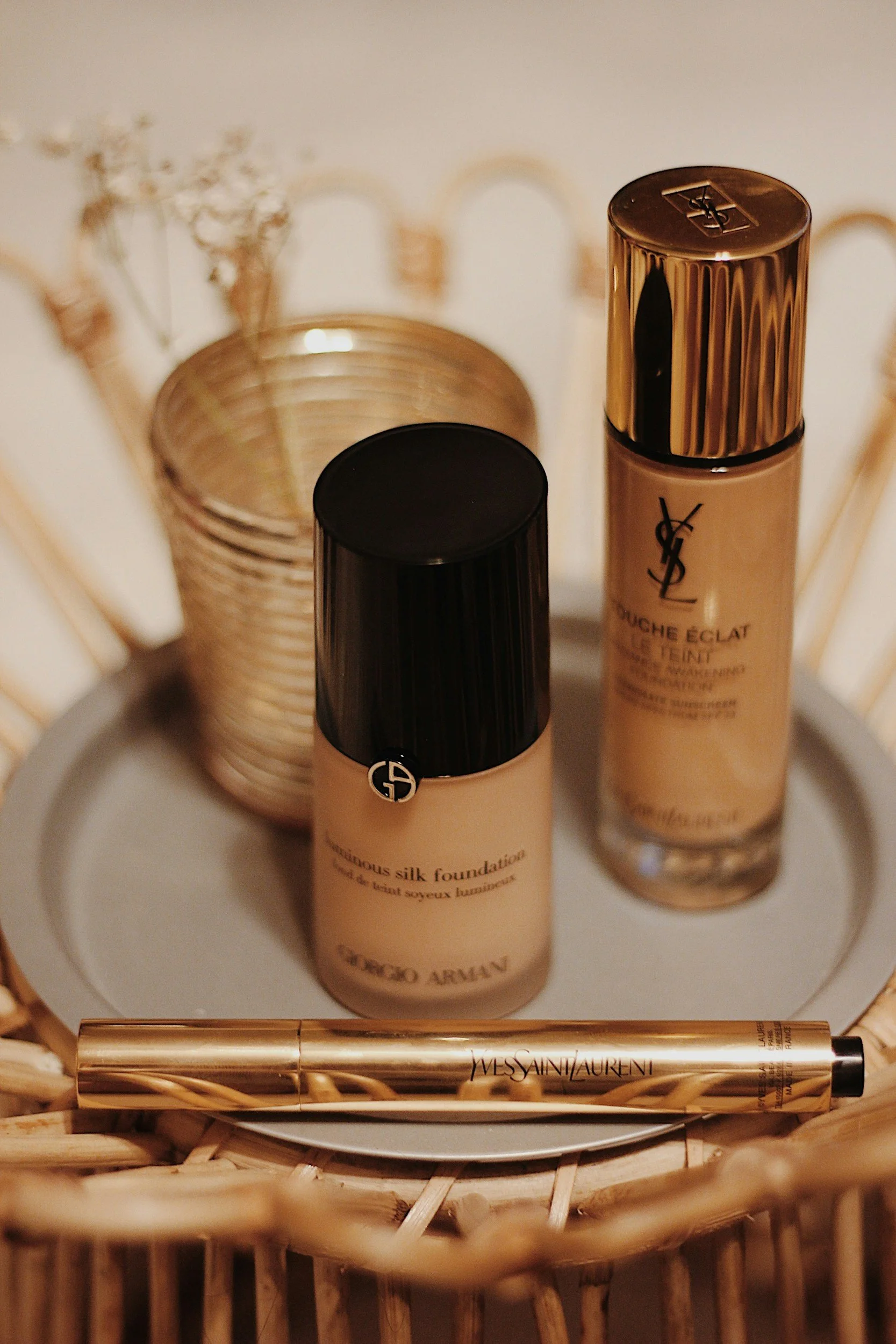 Produits de beauté, notamment un fond de teint Yves Saint Laurent et un fond de teint Giorgio Armani, dans un panier en osier avec un pinceau Yves Saint Laurent.