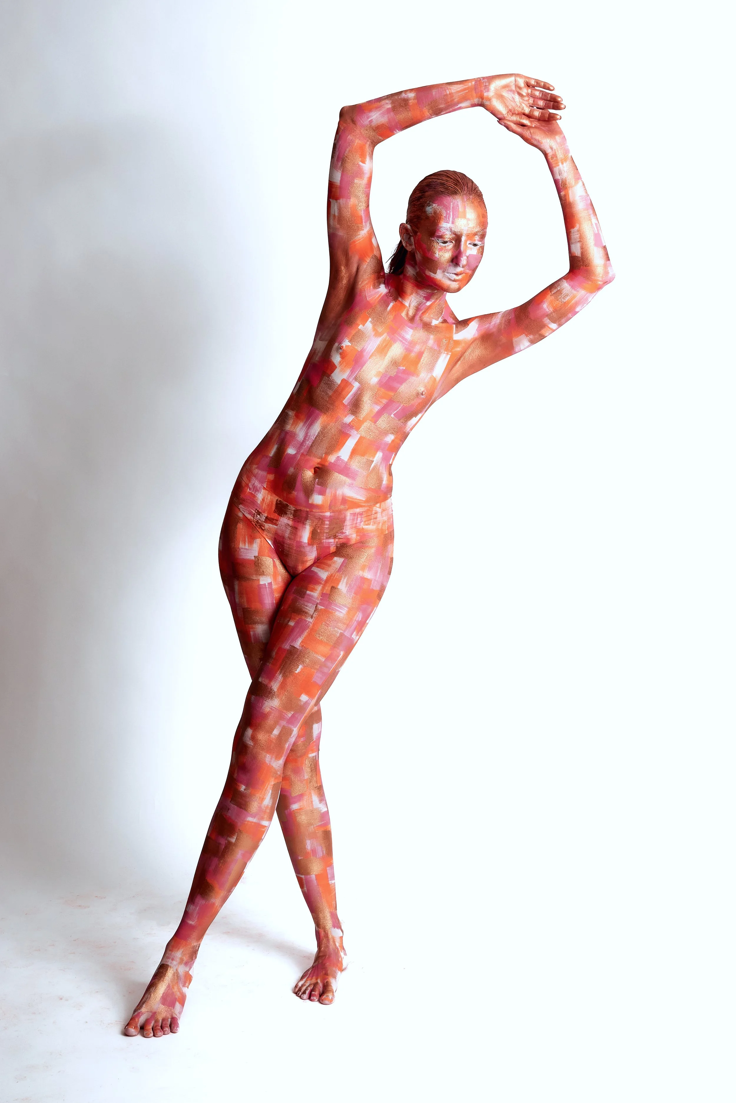 Une femme peinte en couleurs vives et abstraites de bodypainting, posant avec les bras levés au-dessus de sa tête, sur un fond blanc.