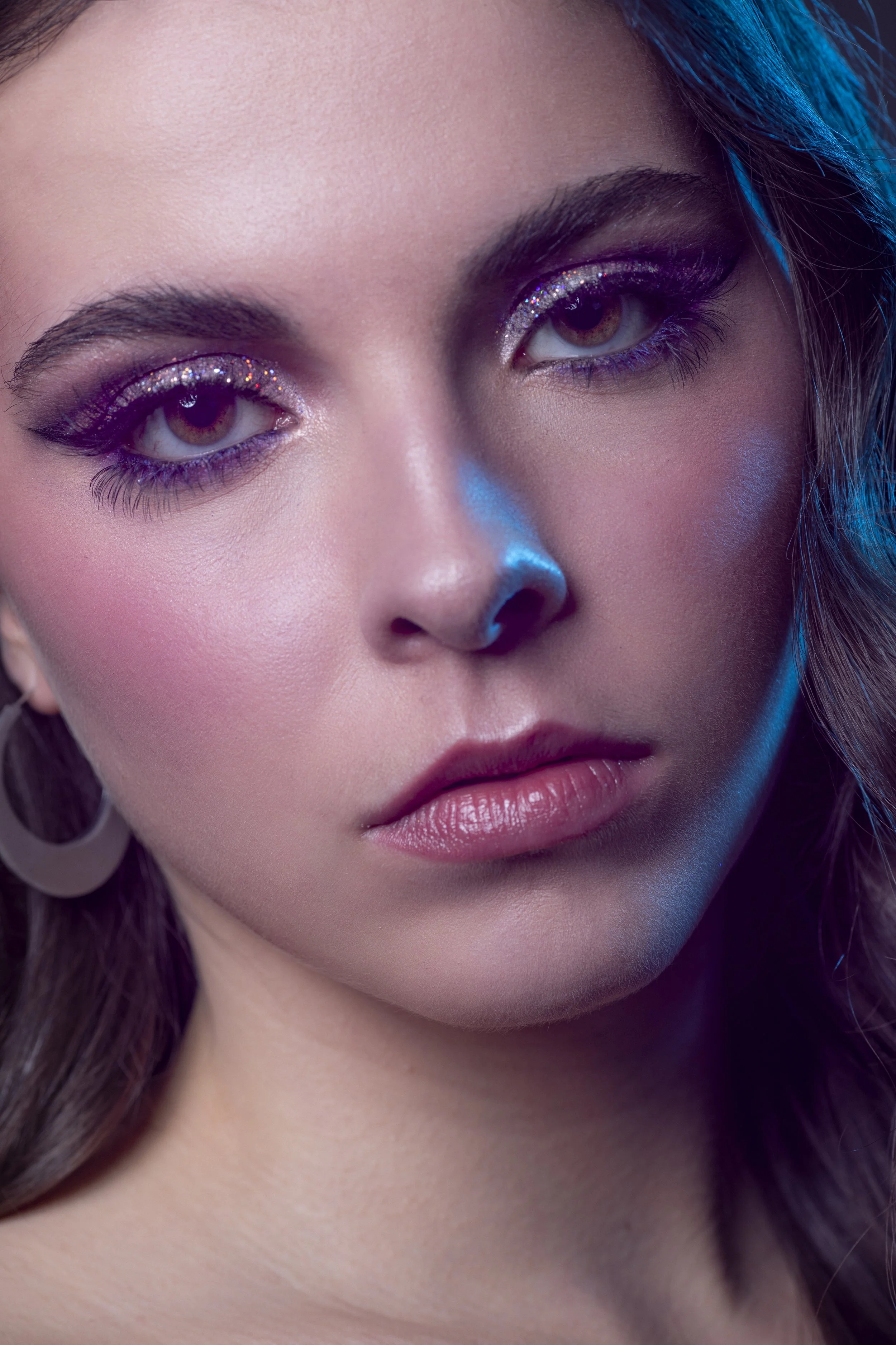 Zoom sur le visage d'une femme avec un maquillage brillant autour des yeux et des lèvres naturelles, cheveux bruns.