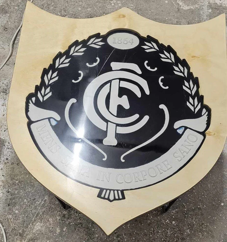 A shield-shaped sign featuring a black and white design with a Latin phrase and emblem, possibly related to a fraternity or organization.