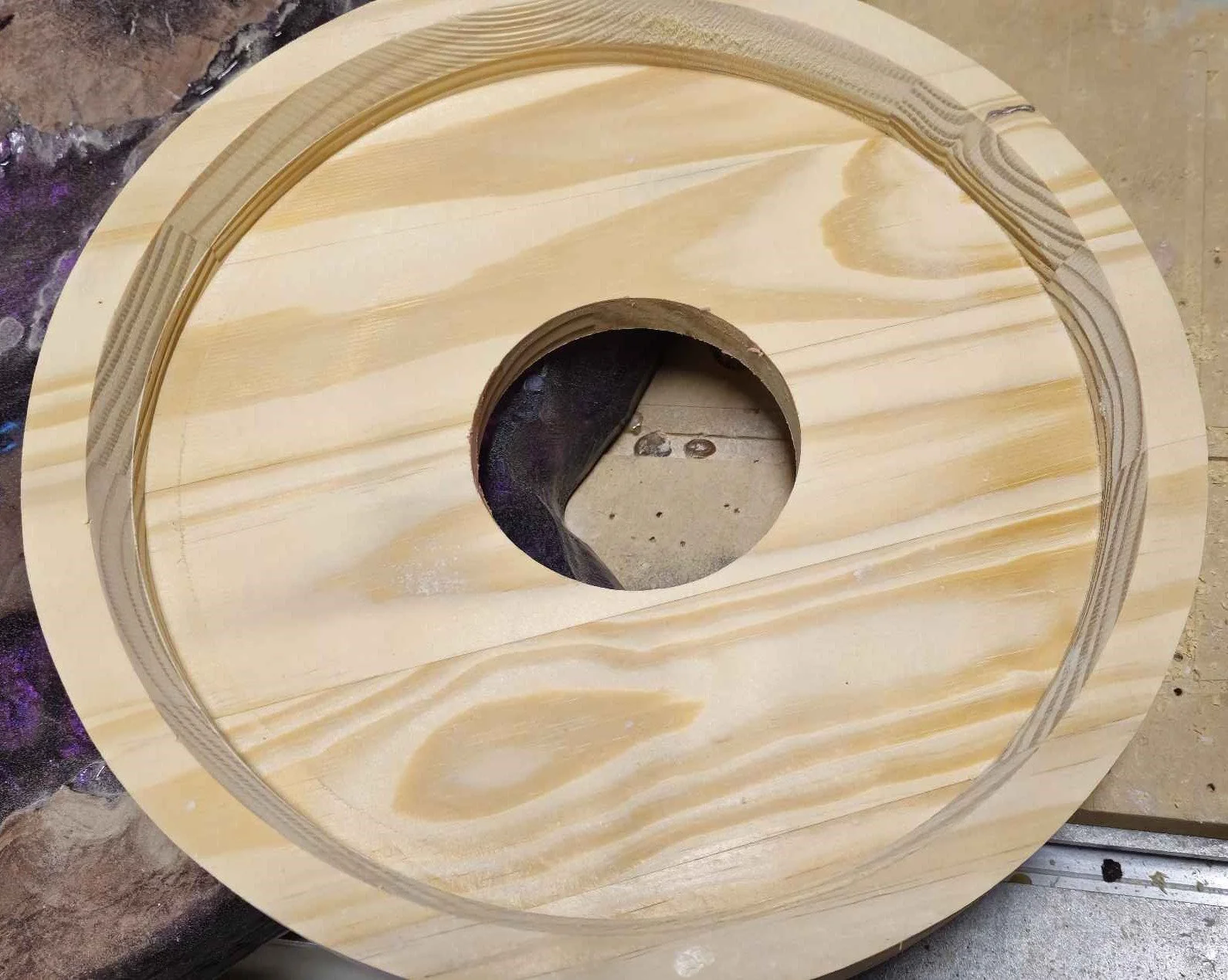 A wooden circular piece with a large round hole in the center, showing a layered pattern along the edges, placed on a work surface.