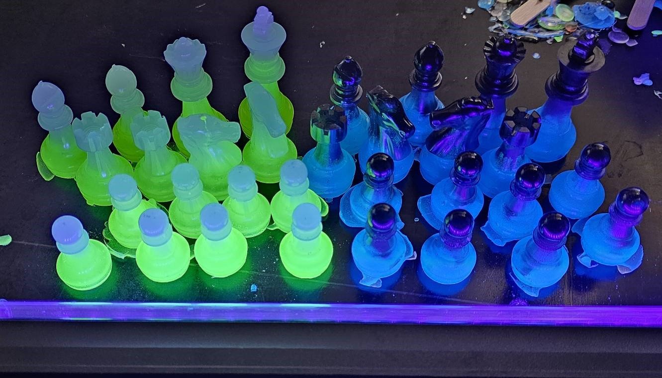 Neon-lit chess pieces arranged as a chessboard, glowing in green and blue under UV lighting.