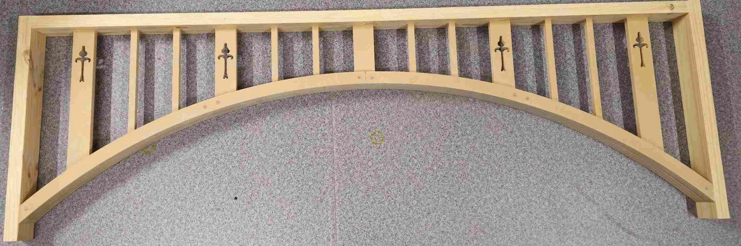 Wooden arch with decorative cross design, lying on a gray floor.