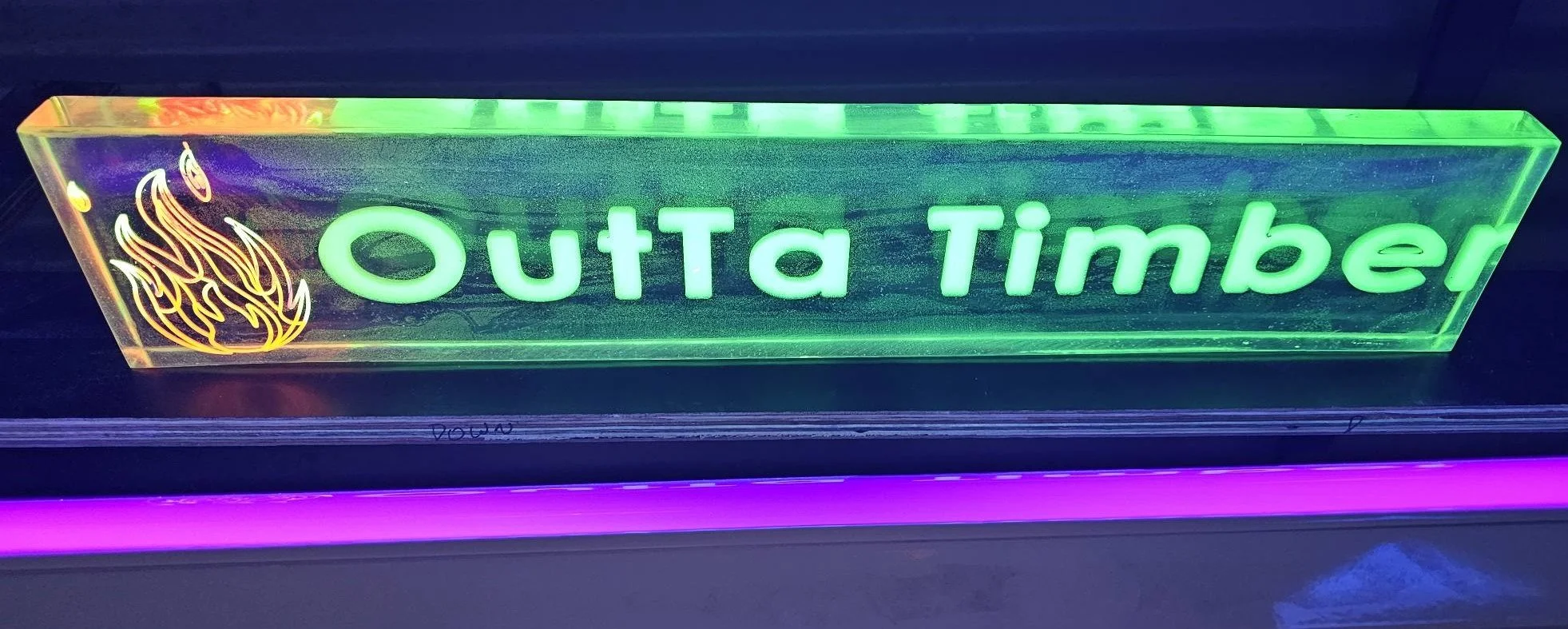 Neon sign with the text 'Outa Timber' in bright green and a flame graphic on the left side.