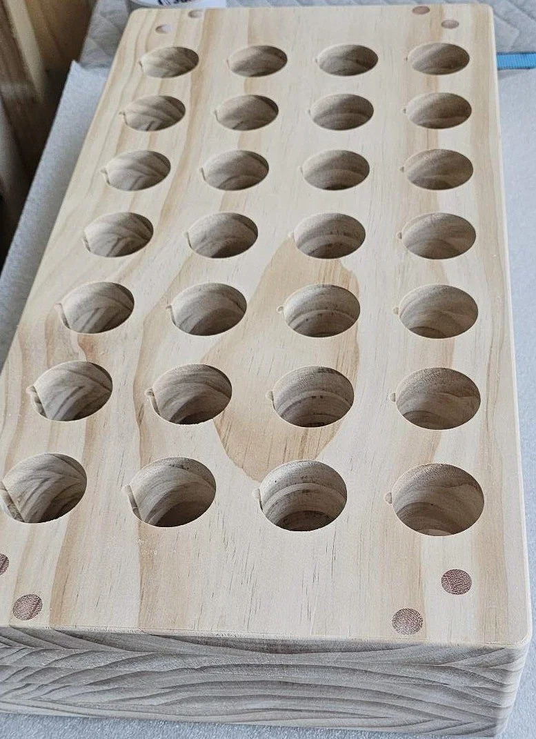 A wooden board with 24 round holes drilled into it, possibly a wine or bottle holder.