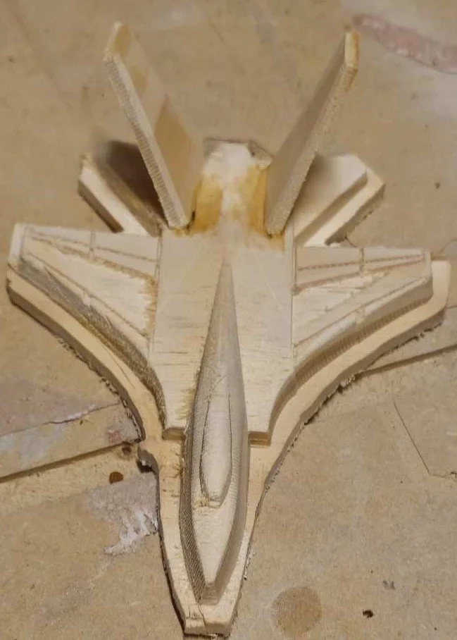 A wooden carving of a stylized f14 tomcat outstretched wings, made from light-colored wood.