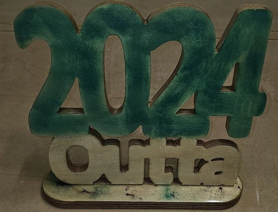 Decorative 2024 New Year sign made of layered wood or acrylic with green and silver colors, reflecting the date 2024.and word outta accross the bottom