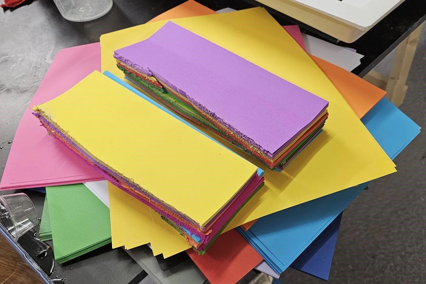Stacks of colorful paper sheets in pink, yellow, purple, green, orange, blue, and white on a table.