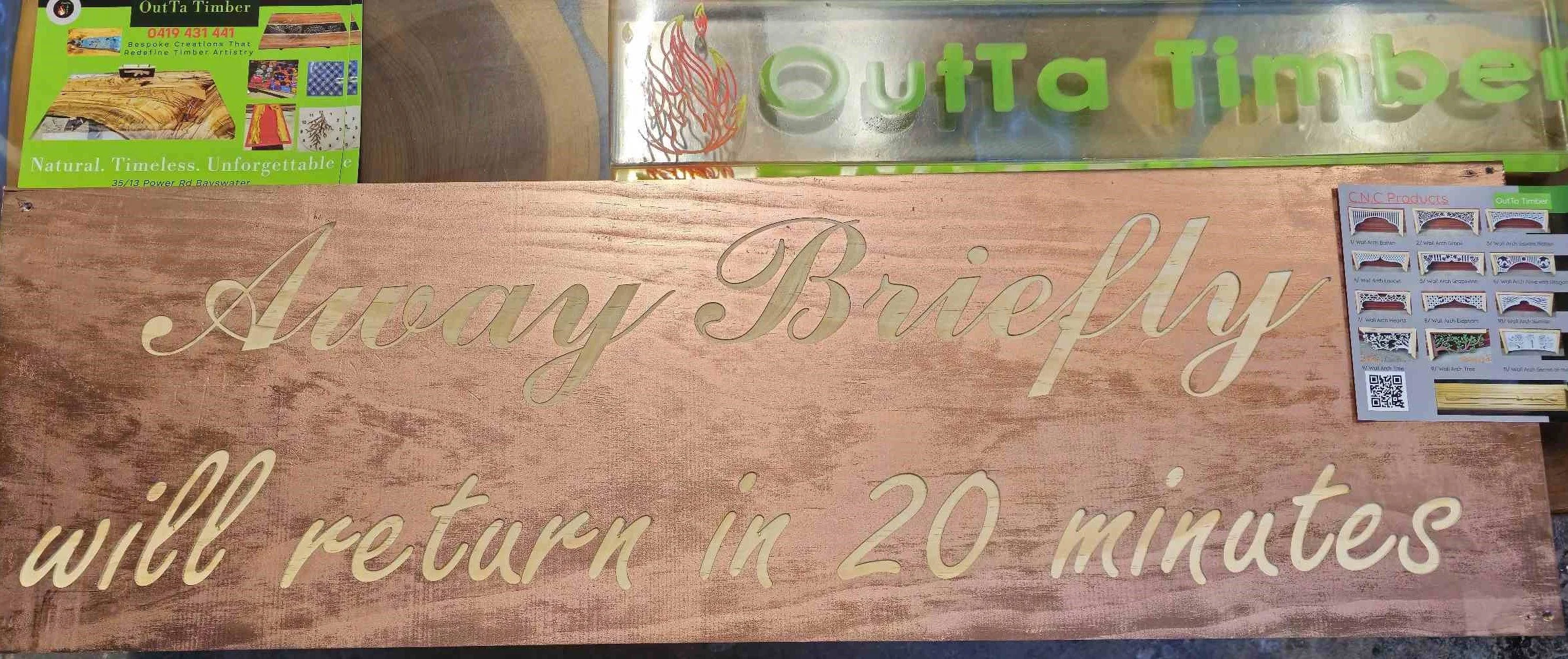 A wooden sign with etched text that reads, 'Away Briefly, will return in 20 minutes.' The sign is displayed on a table or surface with a light-colored backdrop.