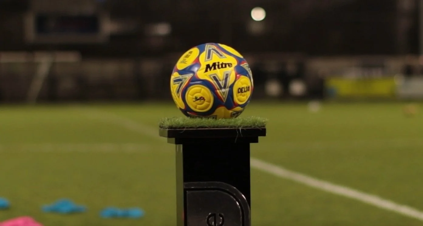 A colorful handball with yellow, blue, and red patterns placed on a small platform on a field, possibly in a sports stadium at night.