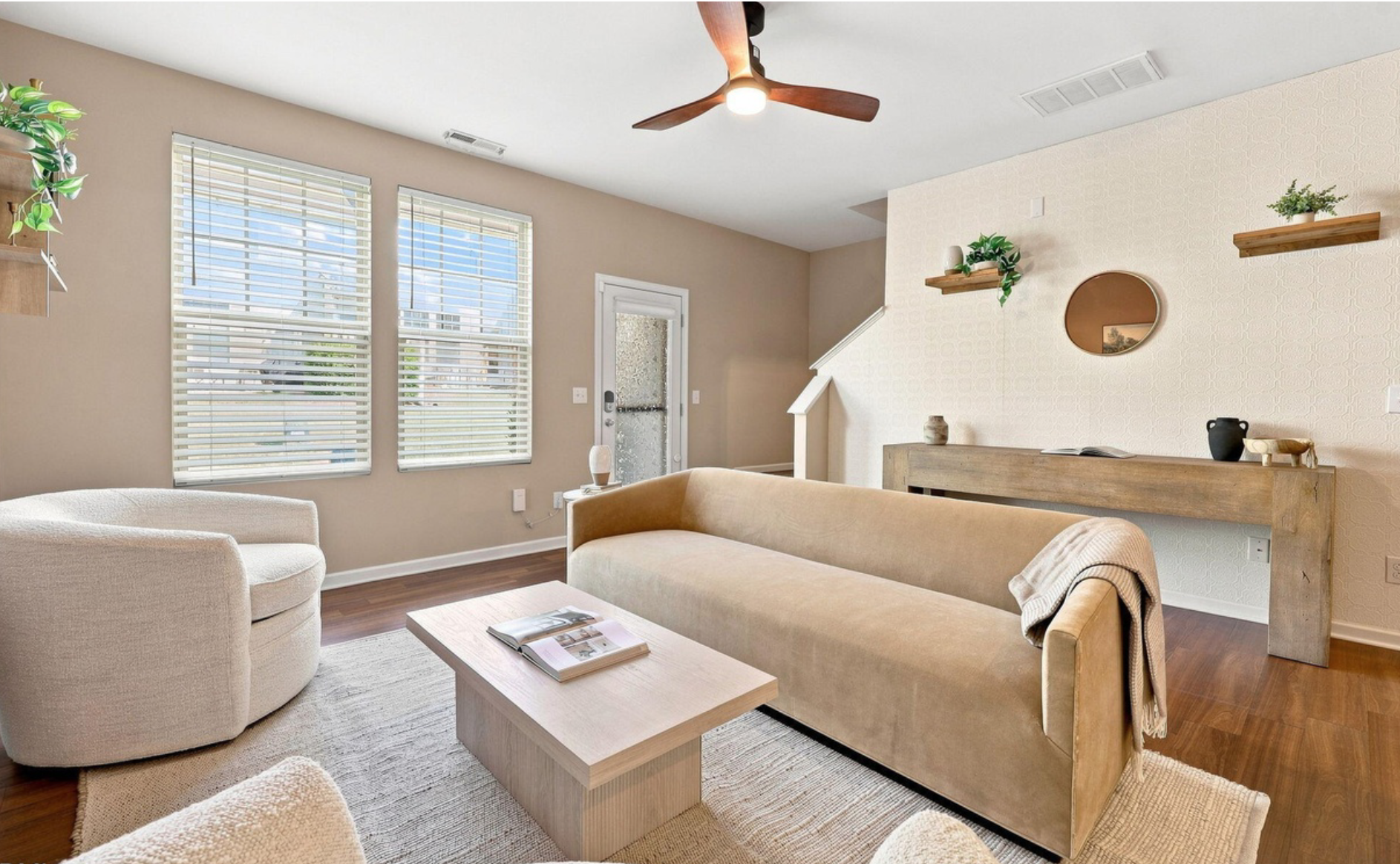 Interior of a living room with a sofa, armchair, coffee table, large windows, and decorative plants, with text overlay announcing a new staging project coming soon at Chapel Hill Staging Co.