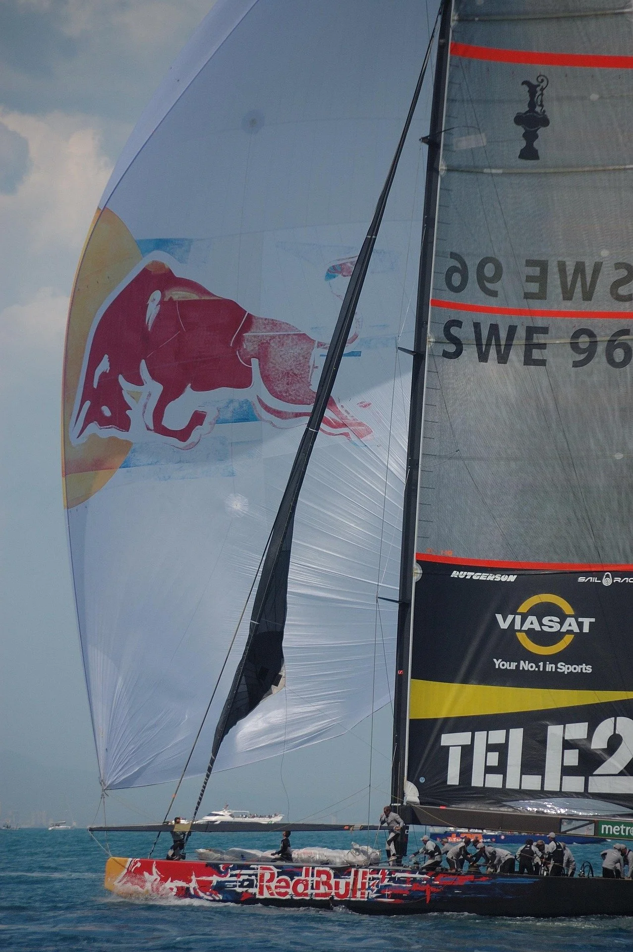 A racing sailboat on the water with large sponsor logos, including Red Bull and Viasat, and a crew working on the deck.