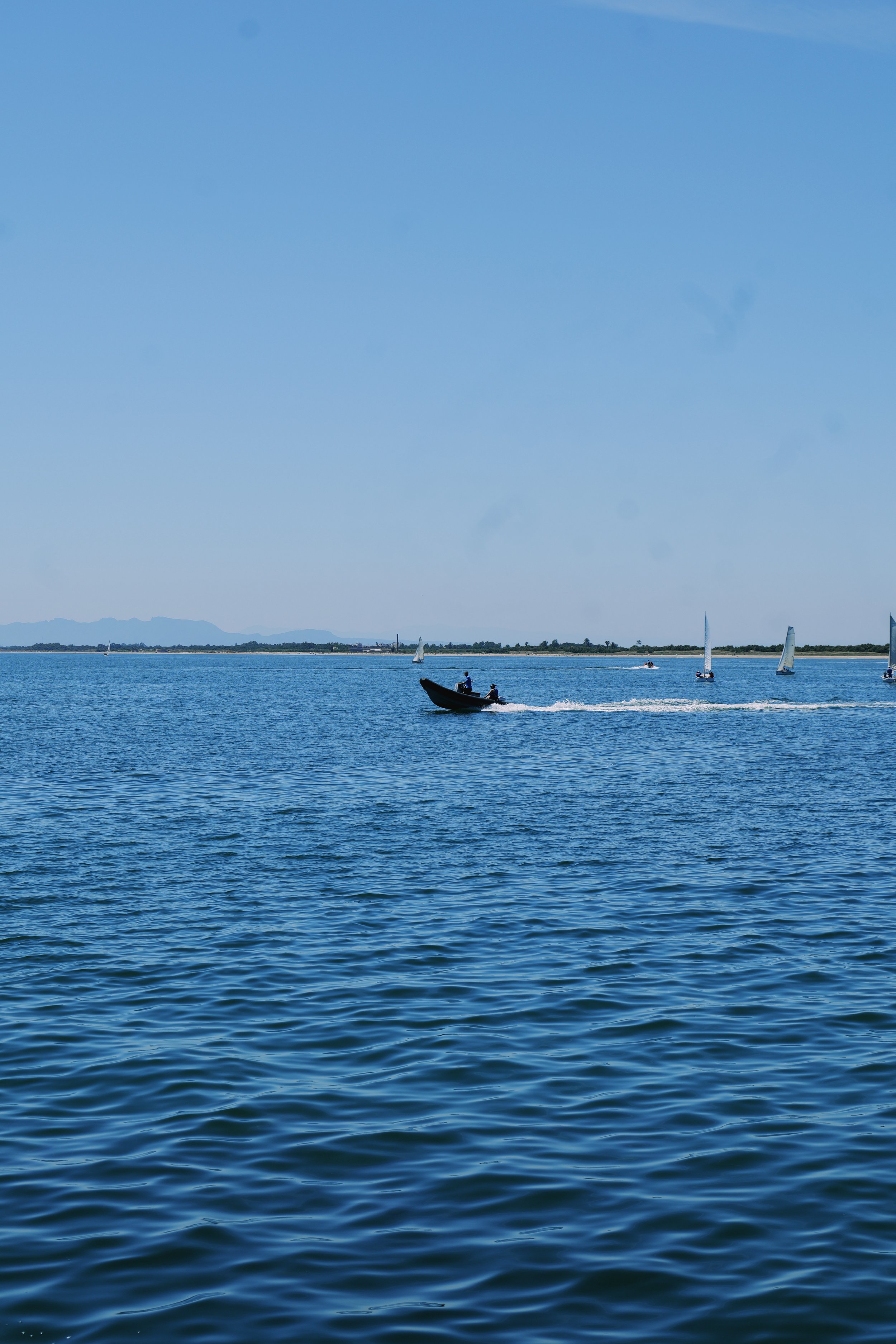 A calm body of water with several sailboats and a motorboat enjoying a clear, sunny day.