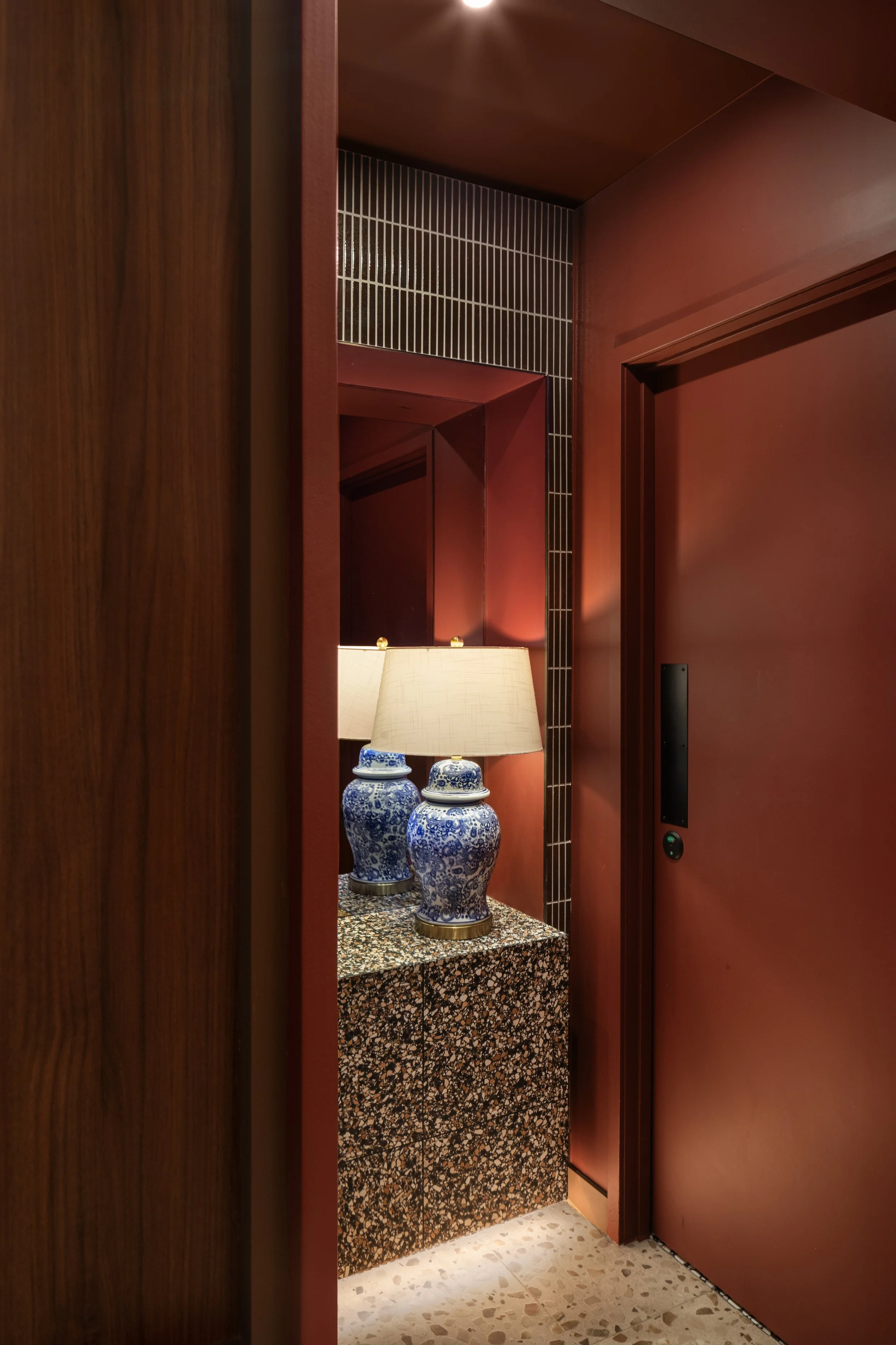 Interior of a building with a marble table holding two blue and white Chinese porcelain vases and a lamp, framed by wooden panels and red walls.