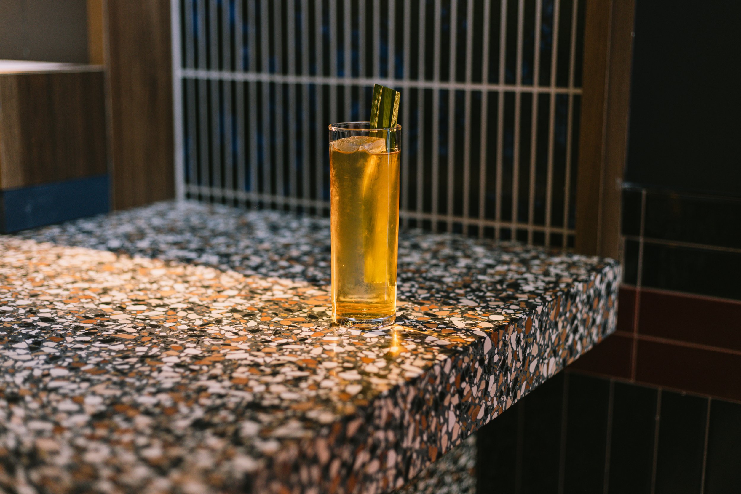 A tall glass of beer with ice cubes and a green-striped straw on a terrazzo countertop.