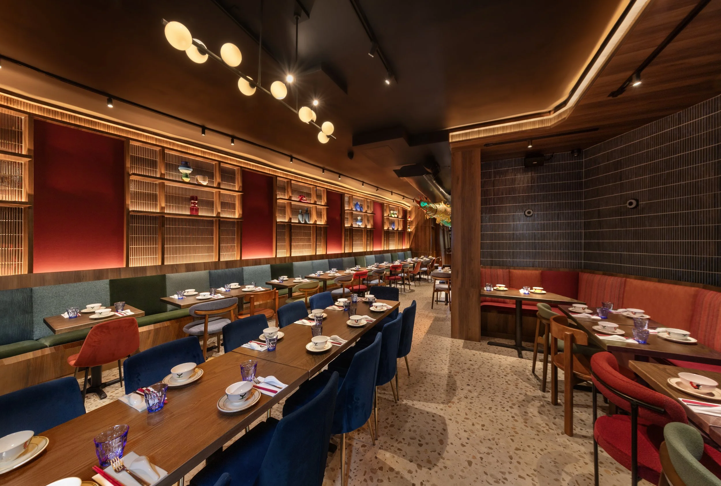Interior of a restaurant with colorful chairs around tables set with plates, cups, and utensils, wood decor, and warm lighting.